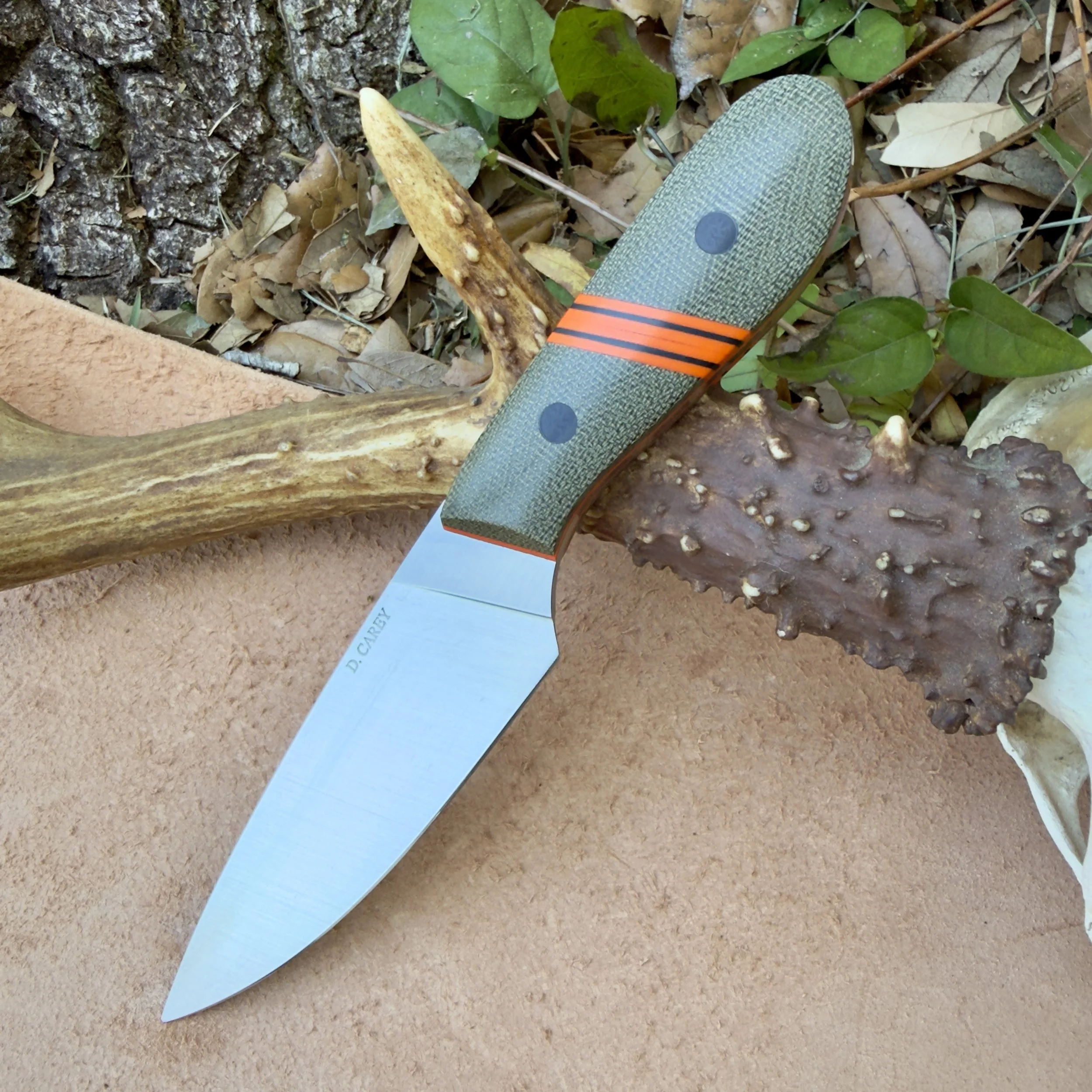 Handmade EDC knife with drop point blade and green micarta handle resting on natural outdoor background