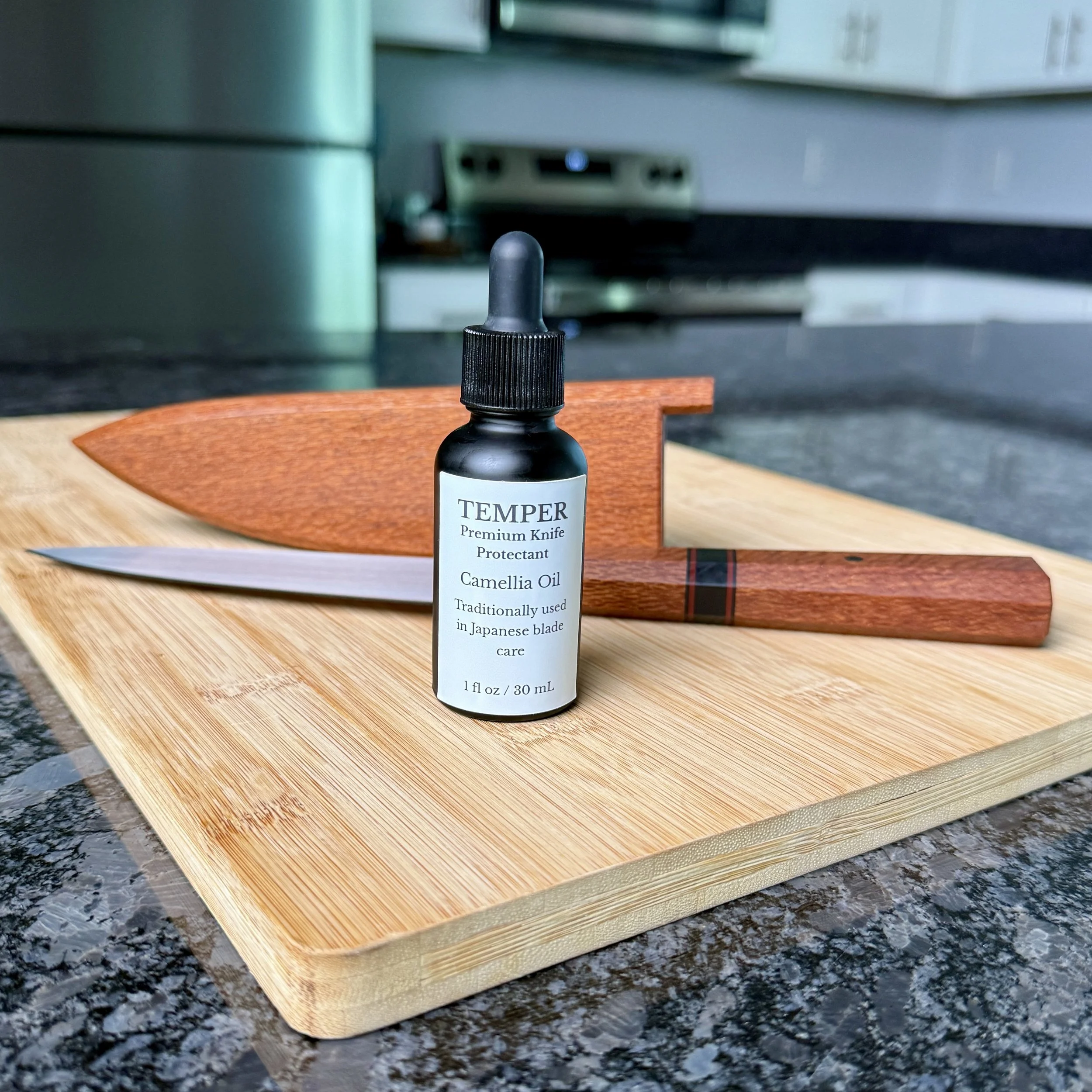 Petty knife with lacewood handle and saya alongside Temper camellia oil on wooden cutting board