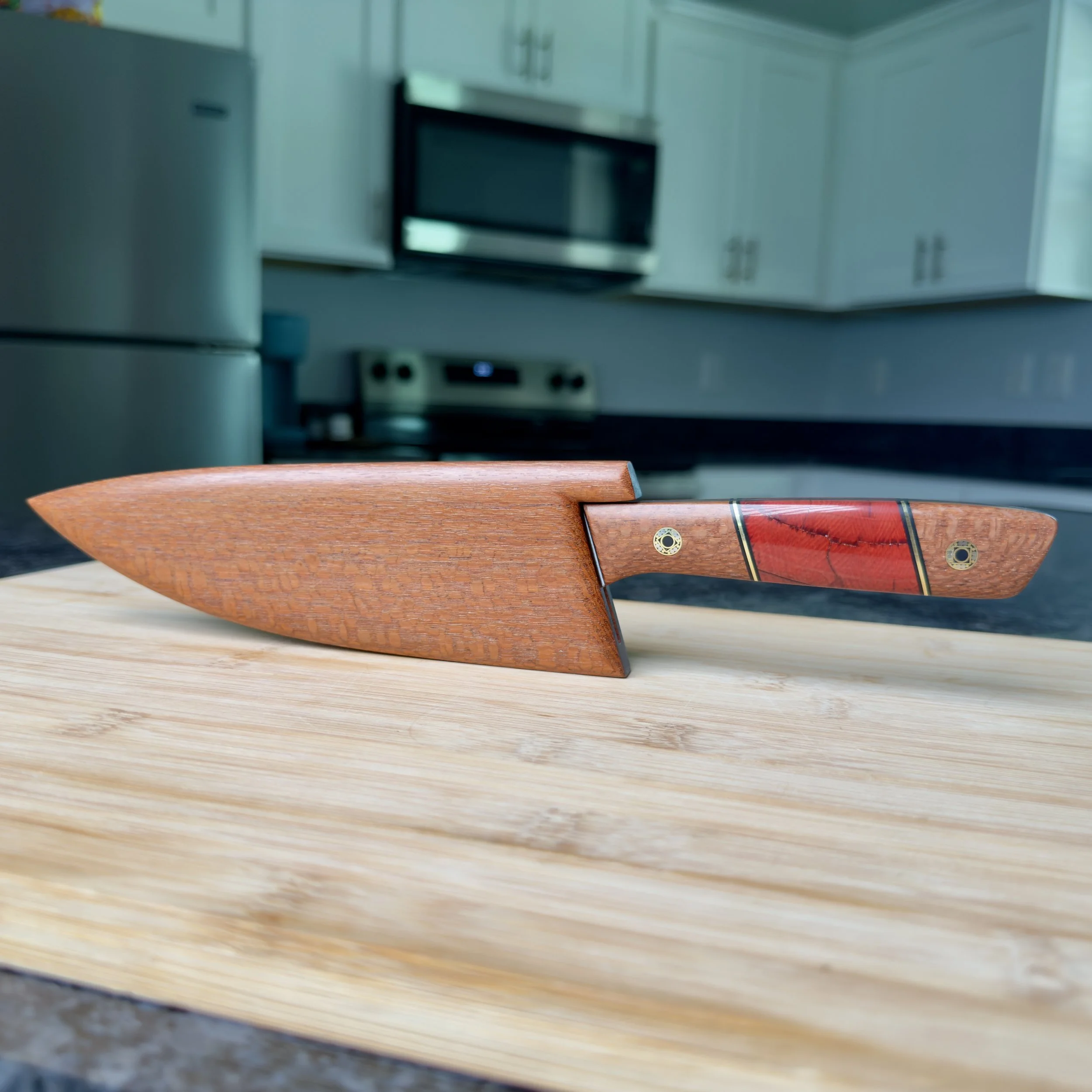 Handmade lacewood chef knife with mammoth tusk handle and wooden saya on kitchen cutting board