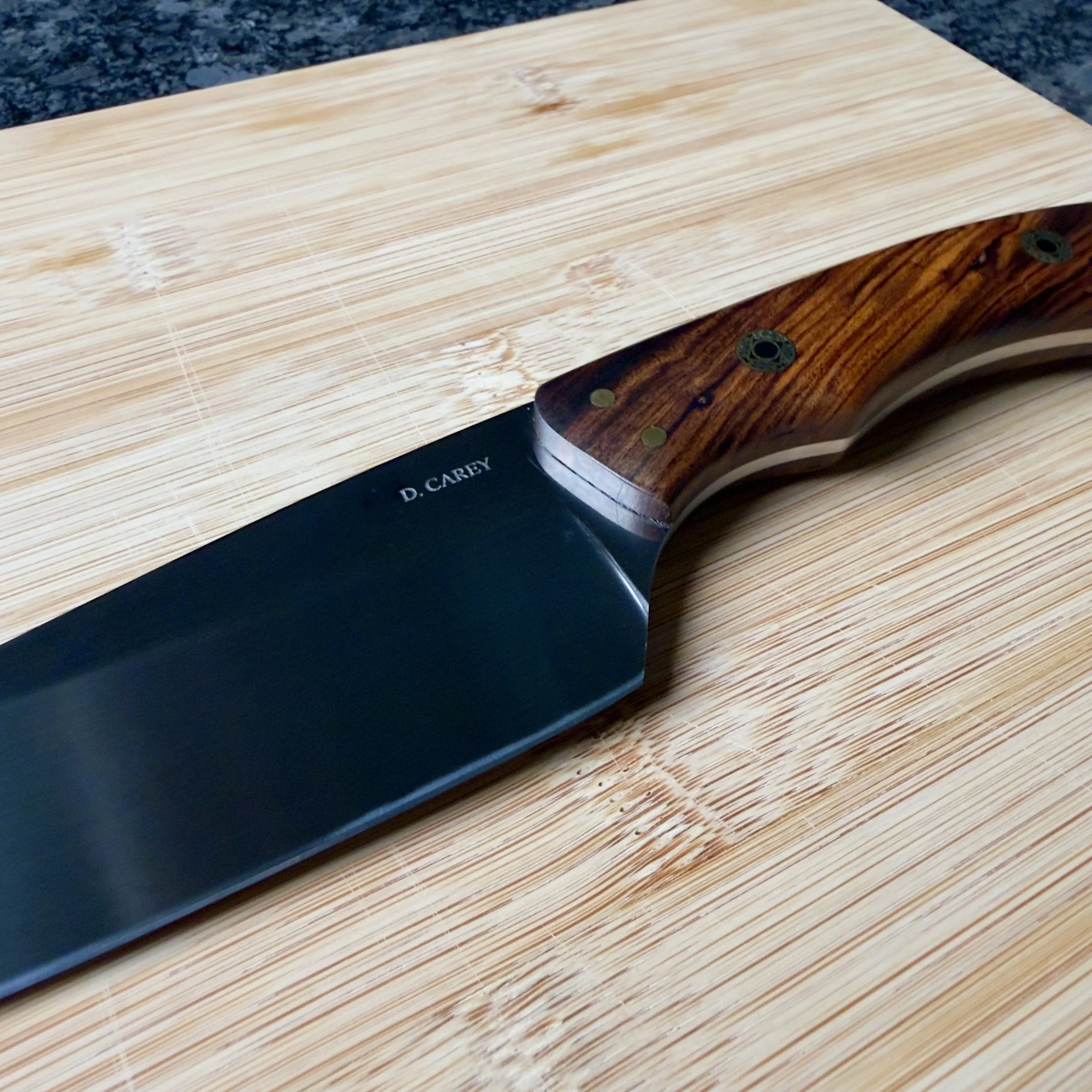 Close-up of the hand-sanded, two-tone satin blade finish and Desert Ironwood handle on a D. Carey handmade chef knife.