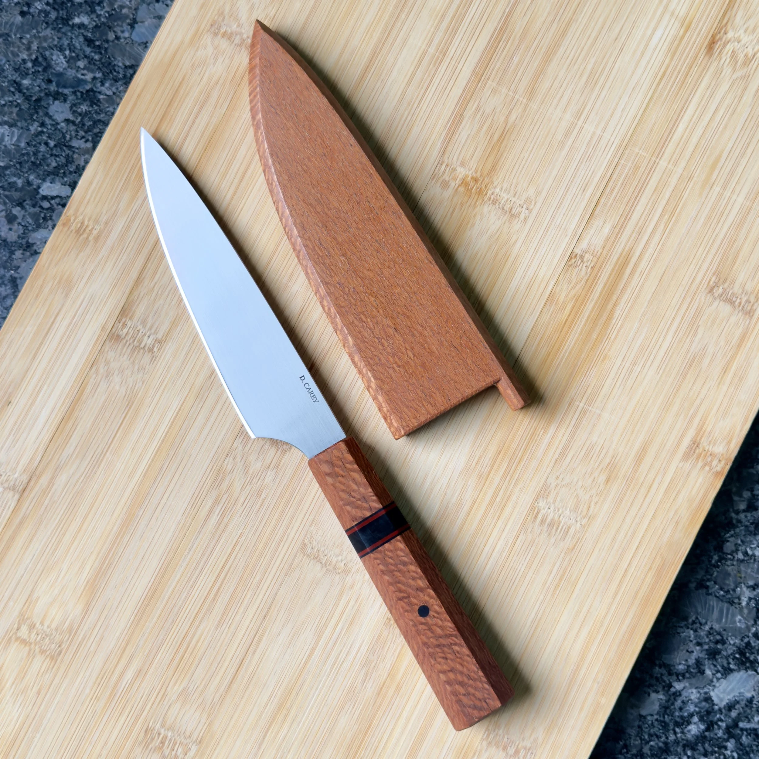 Japanese-style petty knife in 52100 carbon steel with lacewood handle and custom lacewood saya on wood surface