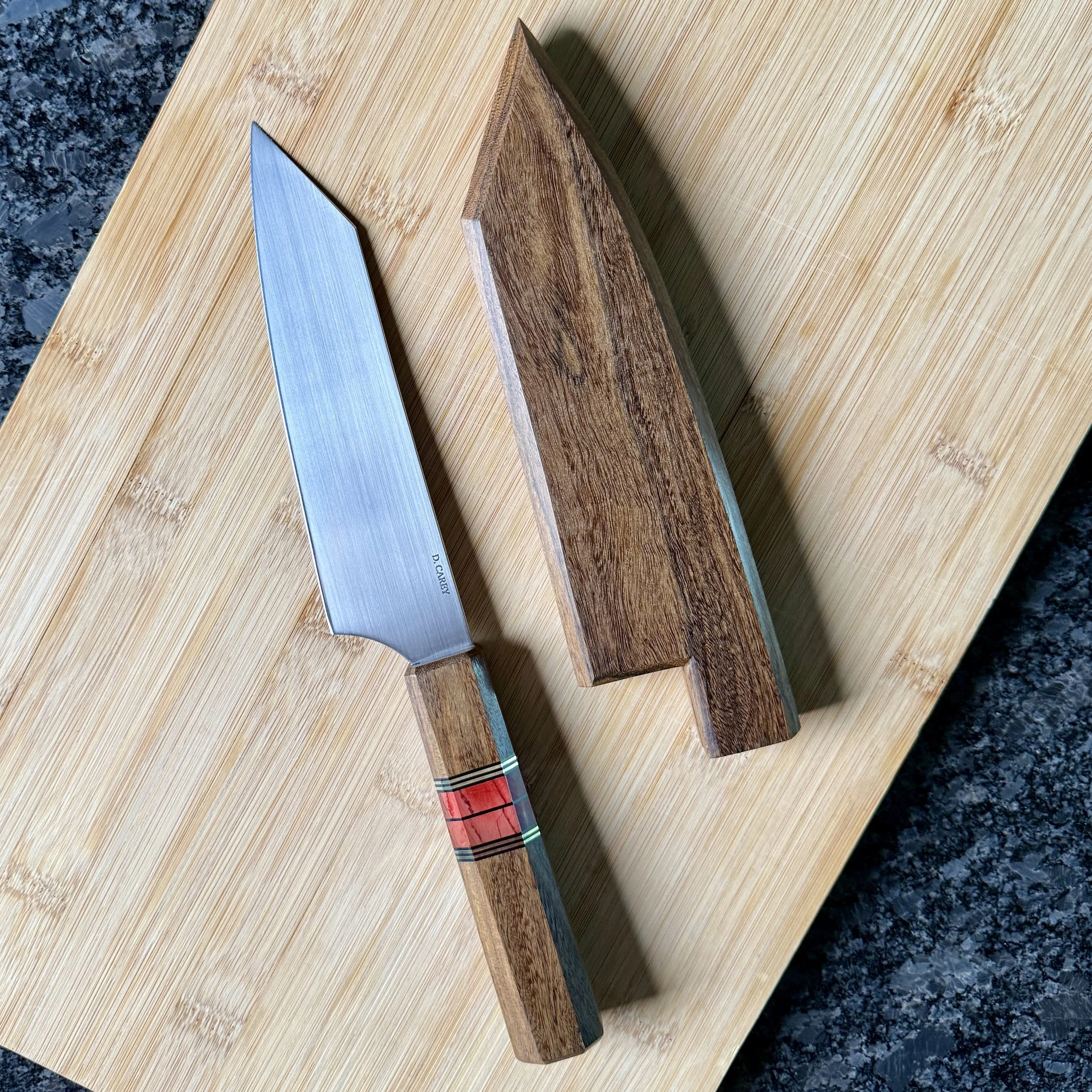Handmade 52100 chef knife with lacewood saya on cutting board, full view