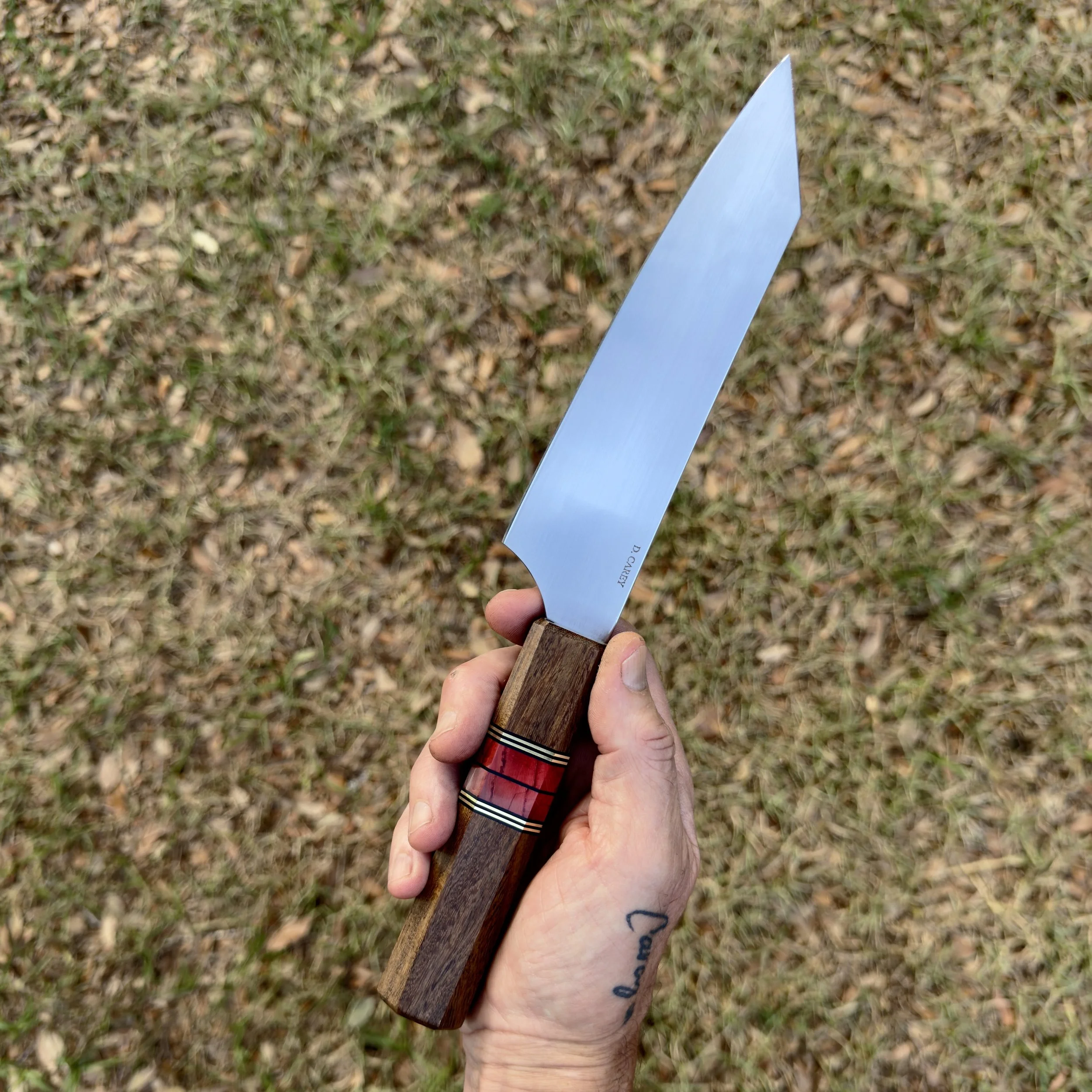 Hand holding 52100 chef knife outdoors, showing blade profile