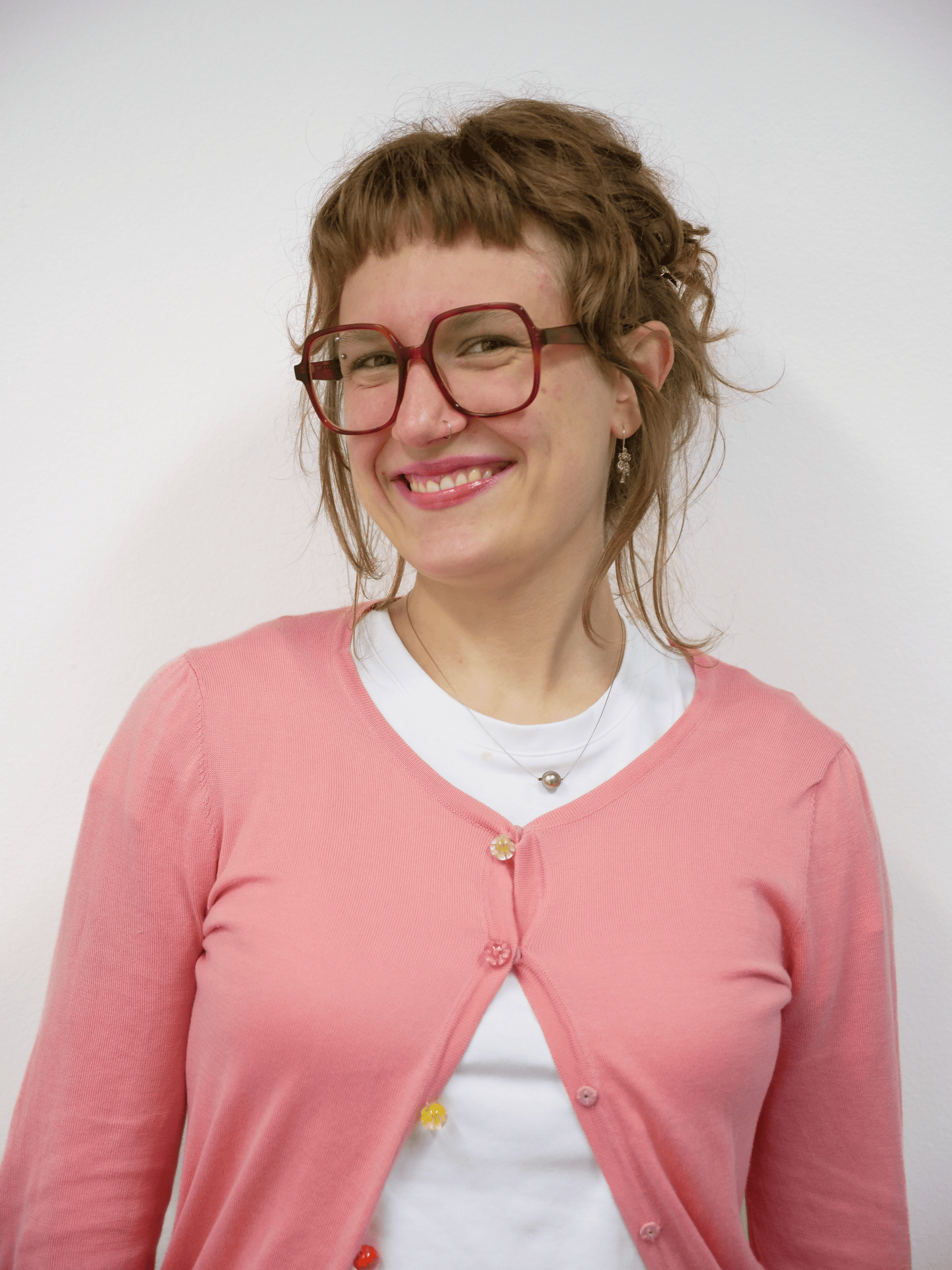 A gif cycling through several portraits of a figure. The figure has short layered brown hair with short bangs. They are wearing large square red glasses, a white tshirt and pink cardigan.