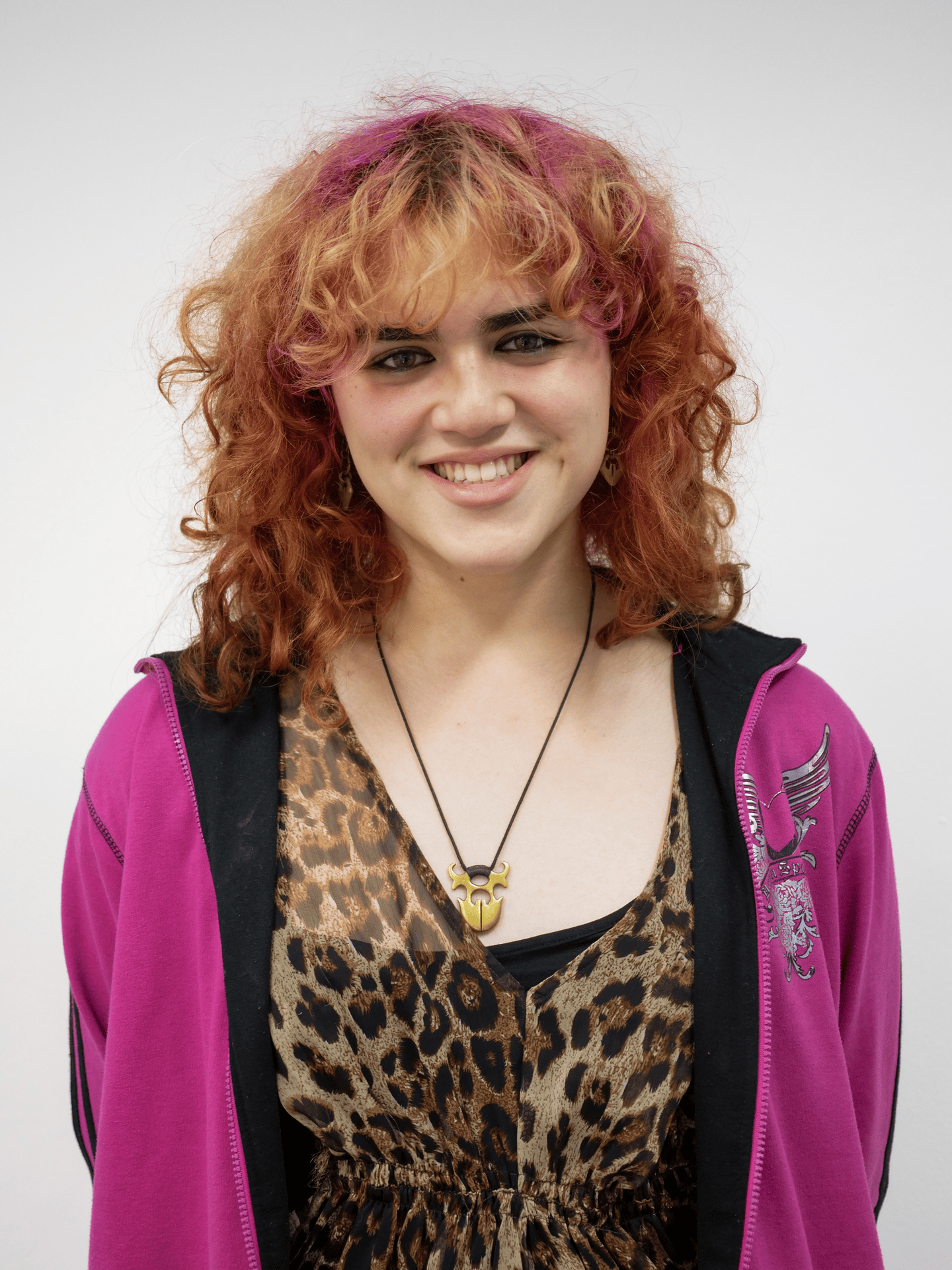 A gif cycling through several portraits of a figure. The figure has shoulder length curly pink hair. They are wearing a sheer leopard print top and a pink hoodie.