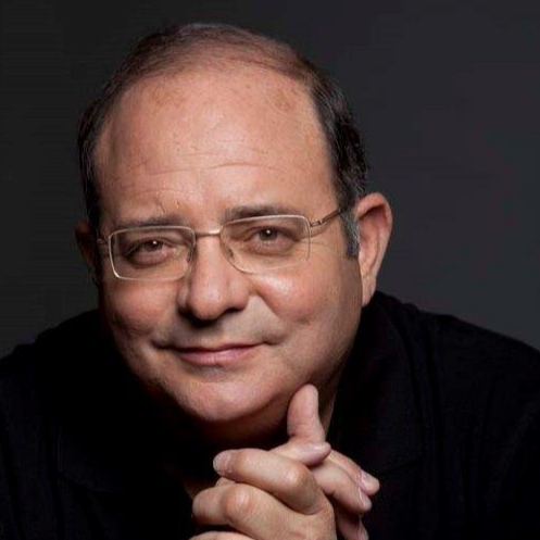 Close-up portrait of a man with glasses, smiling gently against a dark background.