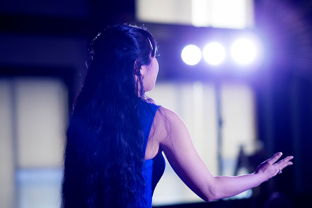 Jacqueline in the benefit show ‘Here I Stand’. Jacqueline stands with her back to the camera and her arms outstretched towards the unseen audience. Photograph: Diamond’s Edge Photography.