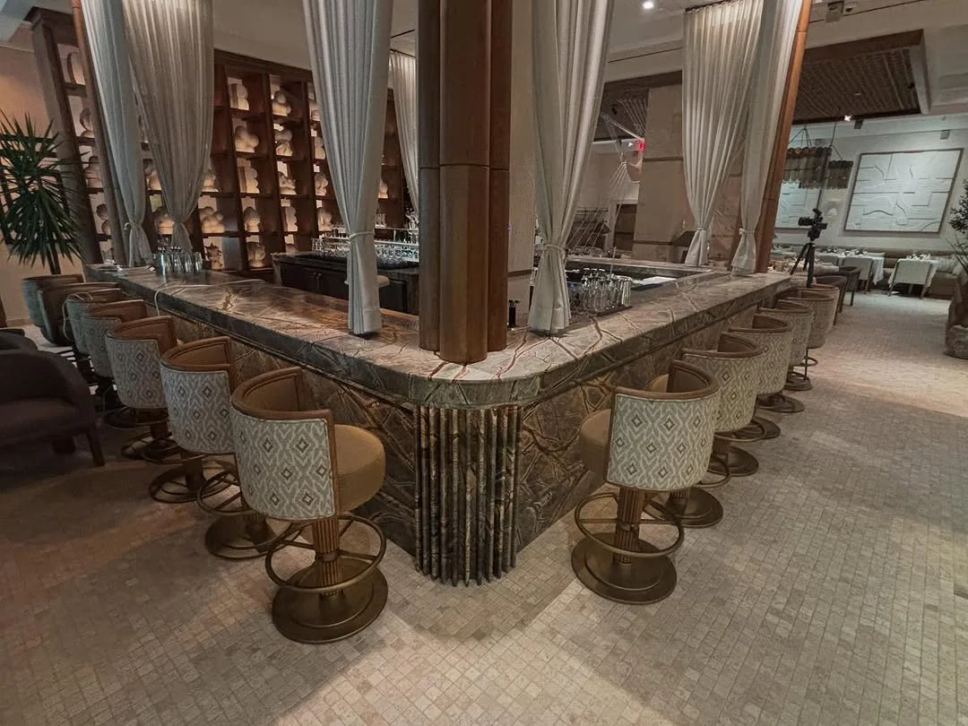 A marble bar counter with upholstered swivel chairs around it, set in a luxurious, contemporary lounge or restaurant interior.
