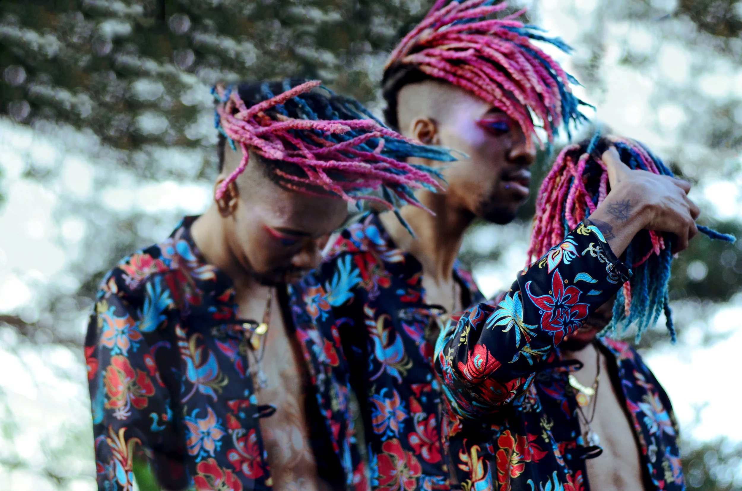 Digitally altered photograph showing a model with red and blue dreadlocks, pink and blue sparkly makeup, wearing a black, red and blue silk floral shirt, headbanging and flipping their hair.