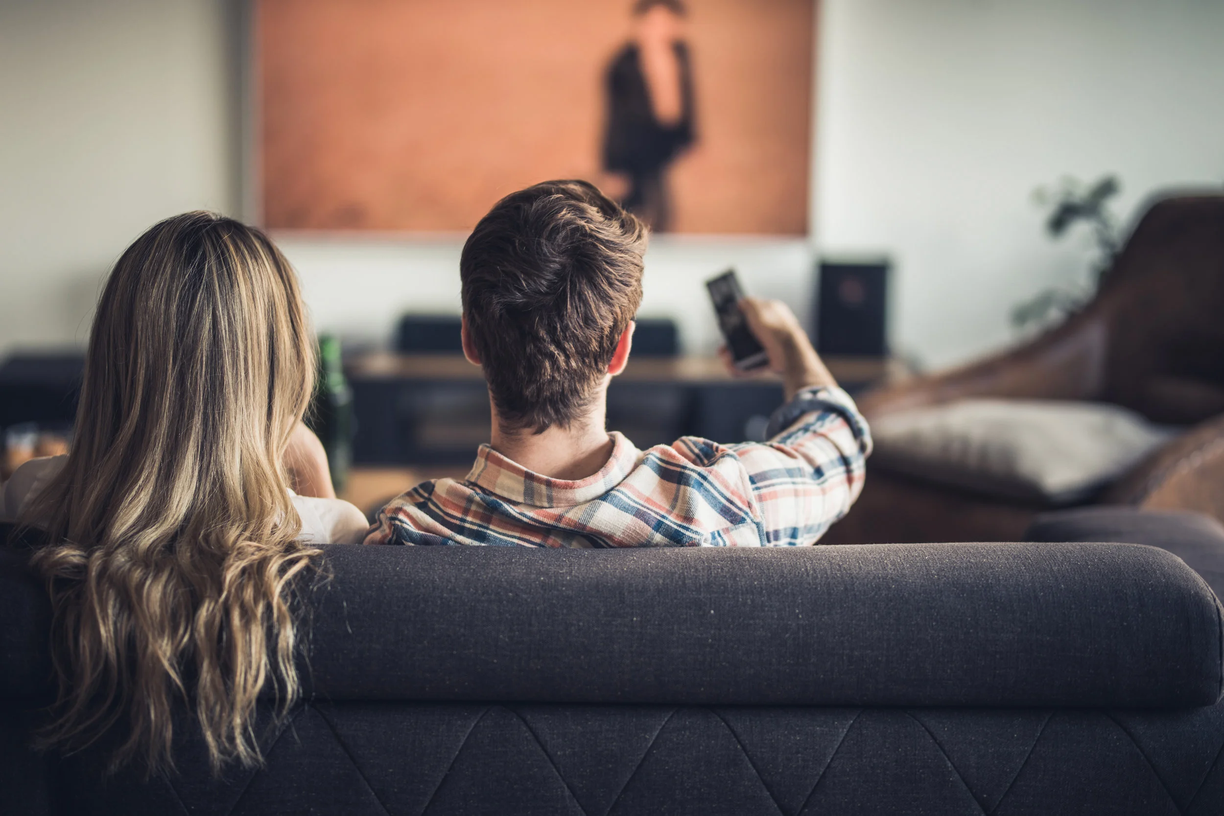 Rear-view-of-a-couple-relaxing-on-sofa-in-the-living-room-and-watching-a-movie-on-TV.-953425192_6720x4480.jpeg