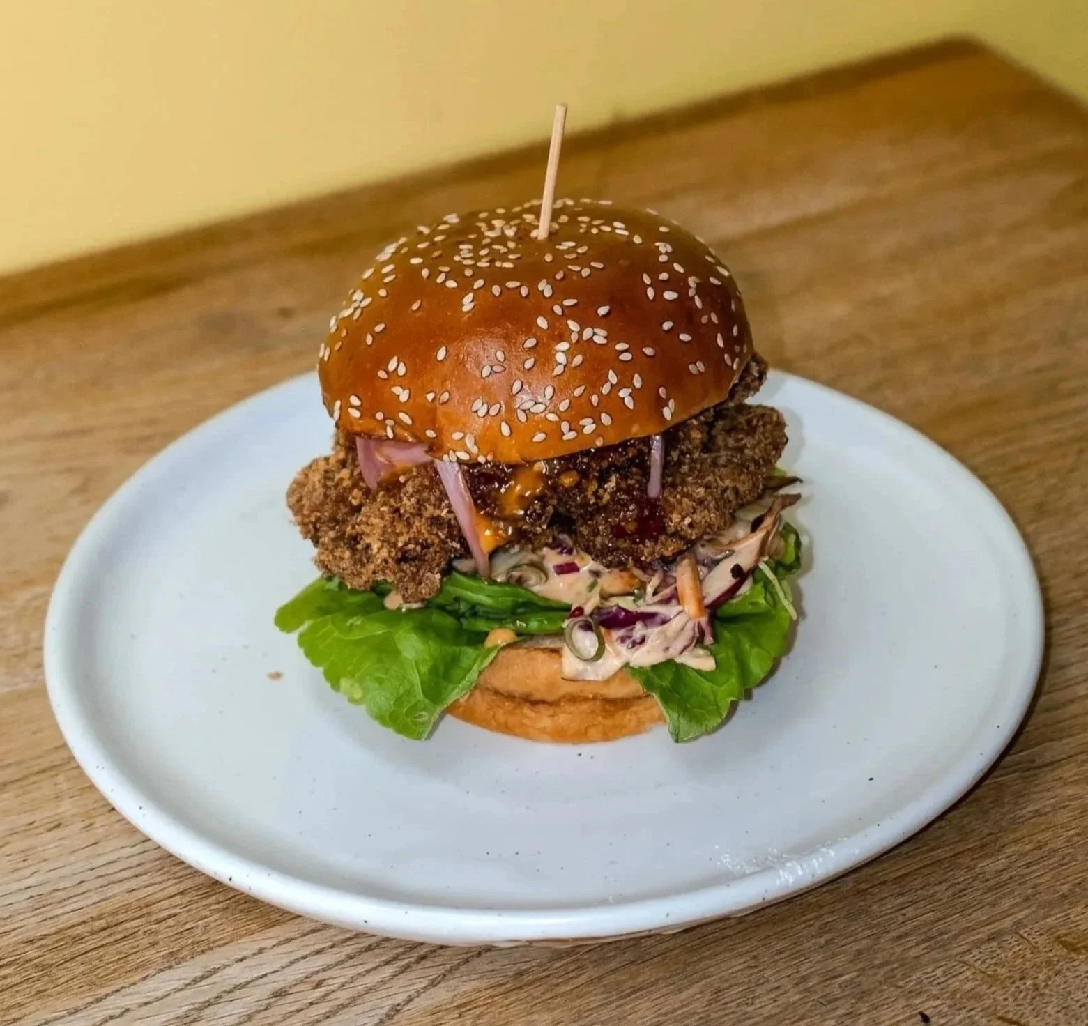 Fried chicken sandwich with lettuce, coleslaw, and sauce in a sesame seed bun on a white plate.