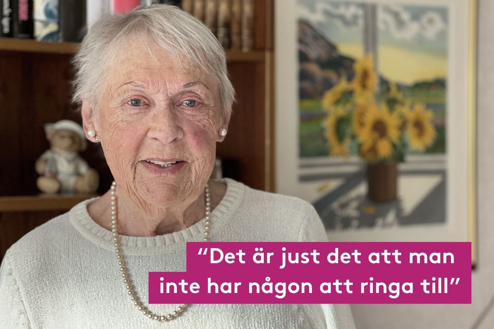 en äldre dam som står framför en brun bokhylla och en tavla som innehåller solrosor. Citatet det är just det att man inte har någon att ringa med vit text och rosa bakgrund.