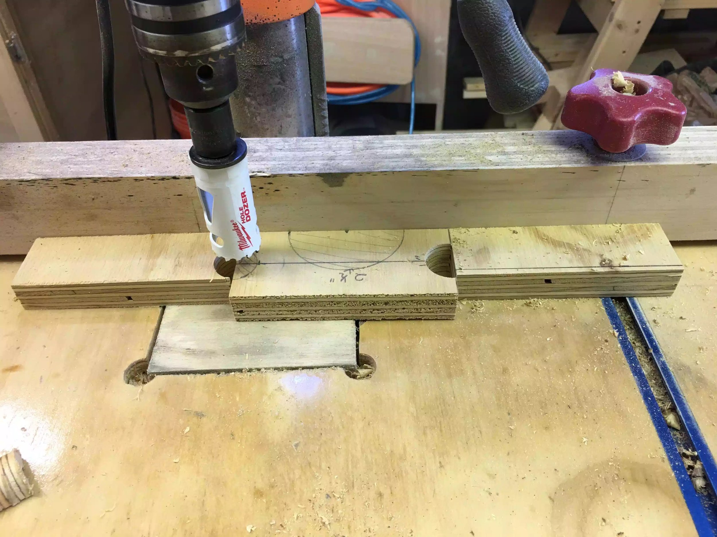 Here is one of the sides in place and to the left and right are 2 sacrificial pieces, he idea was to make sure that the entire cutting surface of the hole saw had something to drill into , thus keeping the hole saw tracking in the downward direction and not chewing up the main piece, and it worked out great. This picture shows me drill the 1” diameter holes on the sides of the feet.