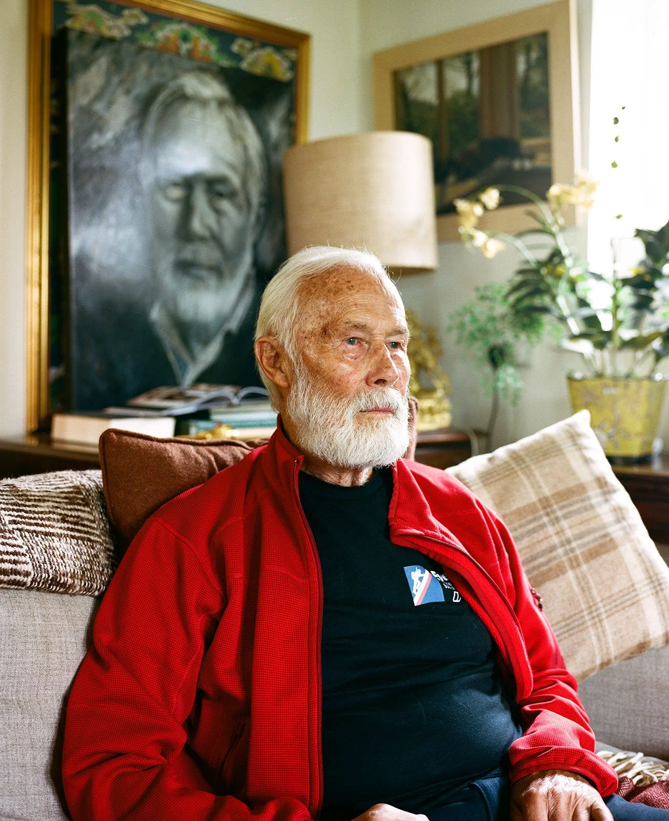 Sir Chris Bonington sitting on a cream sofa, looking toward the window.