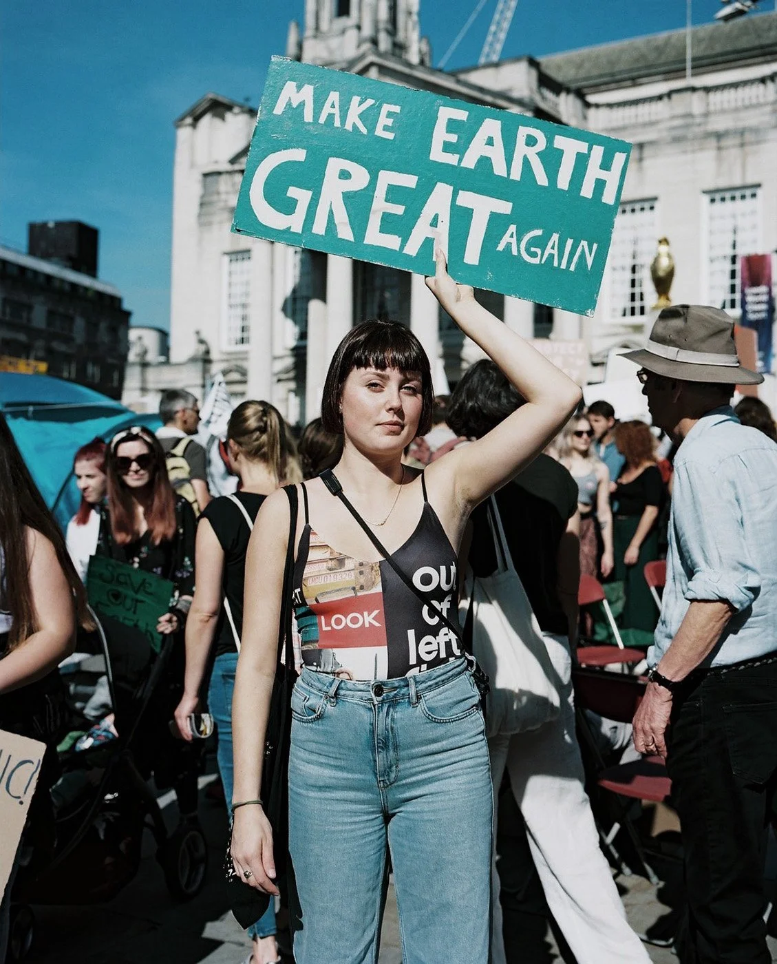 Woman holds a sign reading make earth great again above her head.