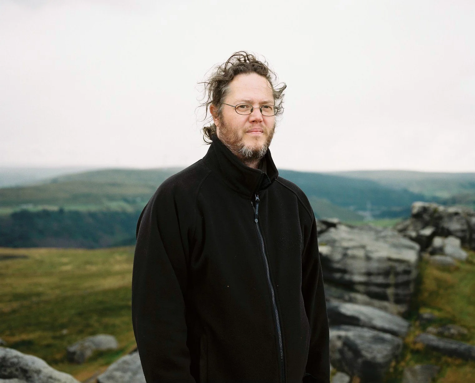 Man standing on moorland with rocky crags behind.