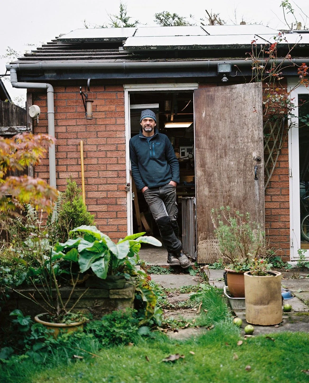 Man standing in a workshop doorway with hands in pockets.