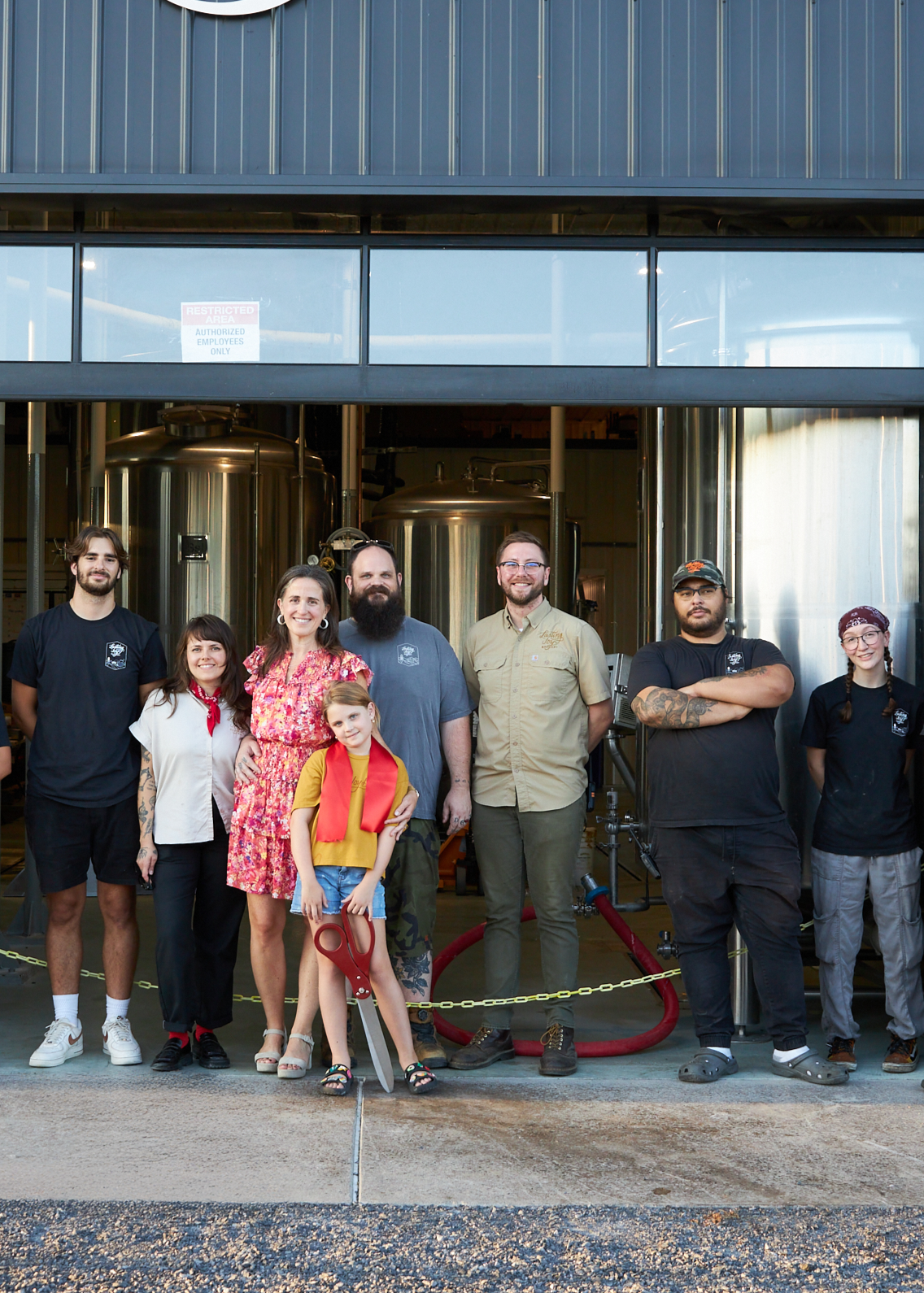 Group of people standing in front of brewing equipment inside a brewery.
