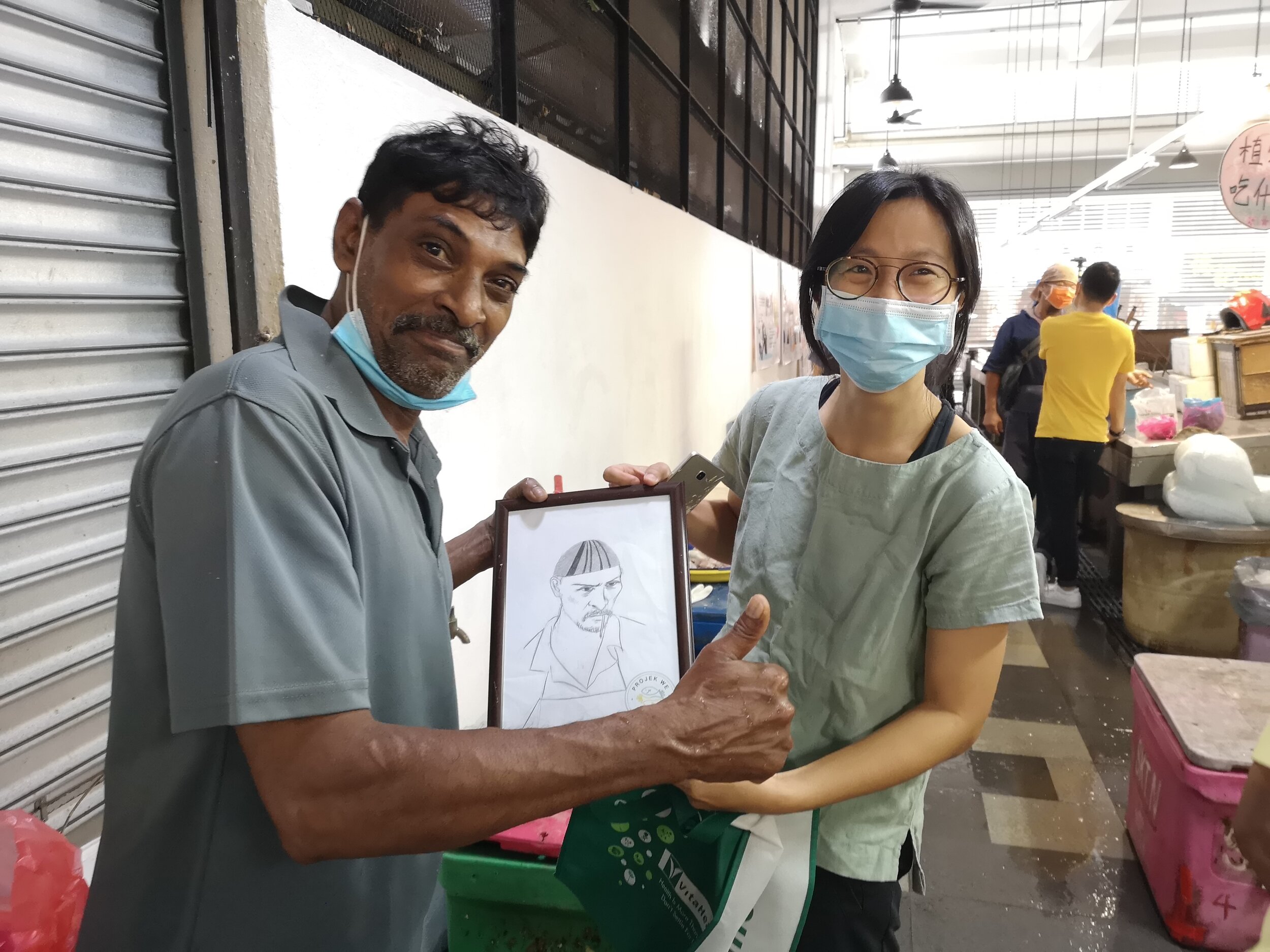  Happy seafood vendor, Razak, with his framed portrait handrawn and presented by the trainee artist herself 