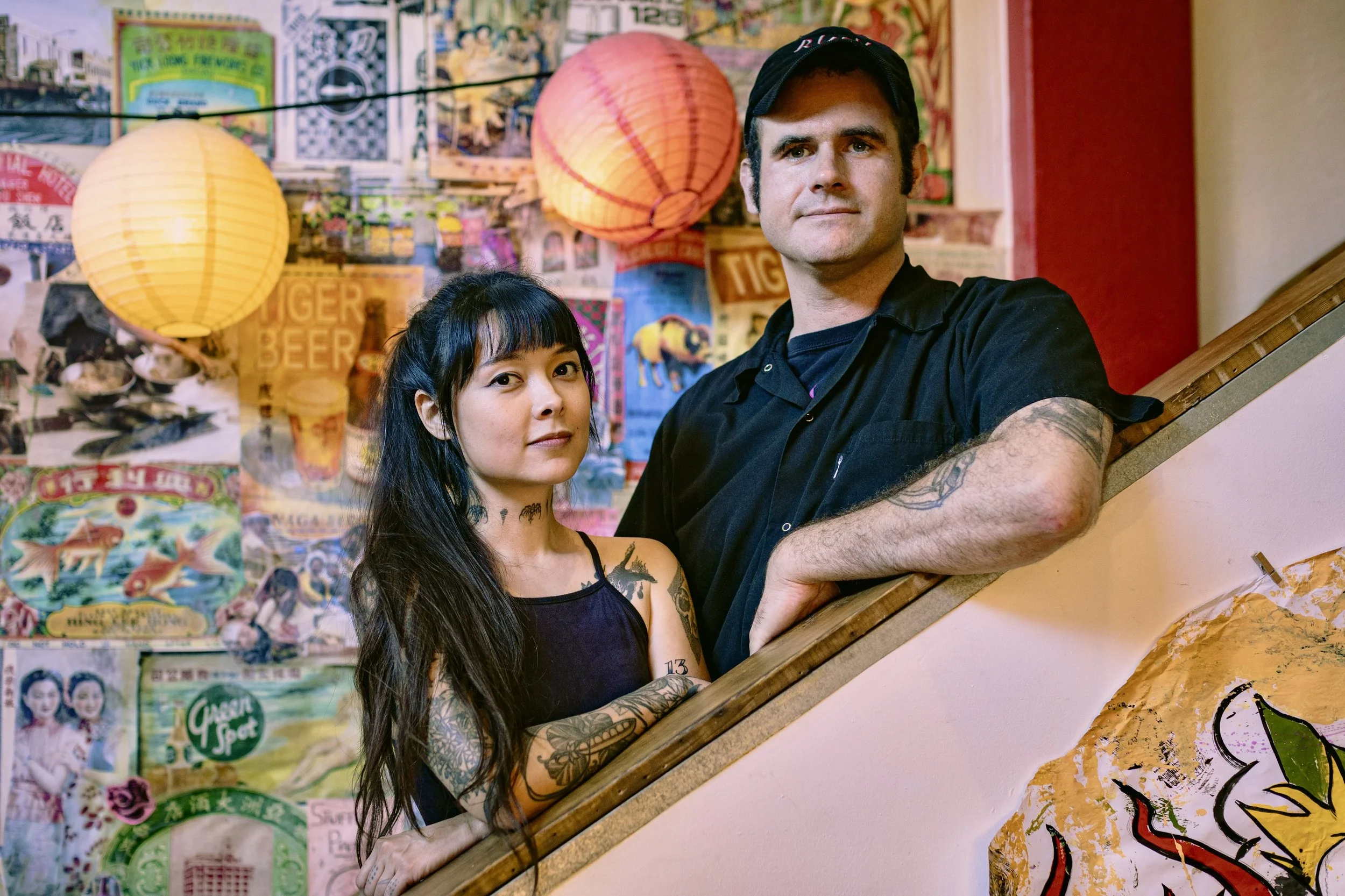 Lion Dance Cafe owners C-Y and Shane smiling at the camera from the restaurant's colorful staircase.