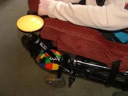 a yellow switch on a black metal rod next to a chair. A person’s arm rests on the arm of the chair.
