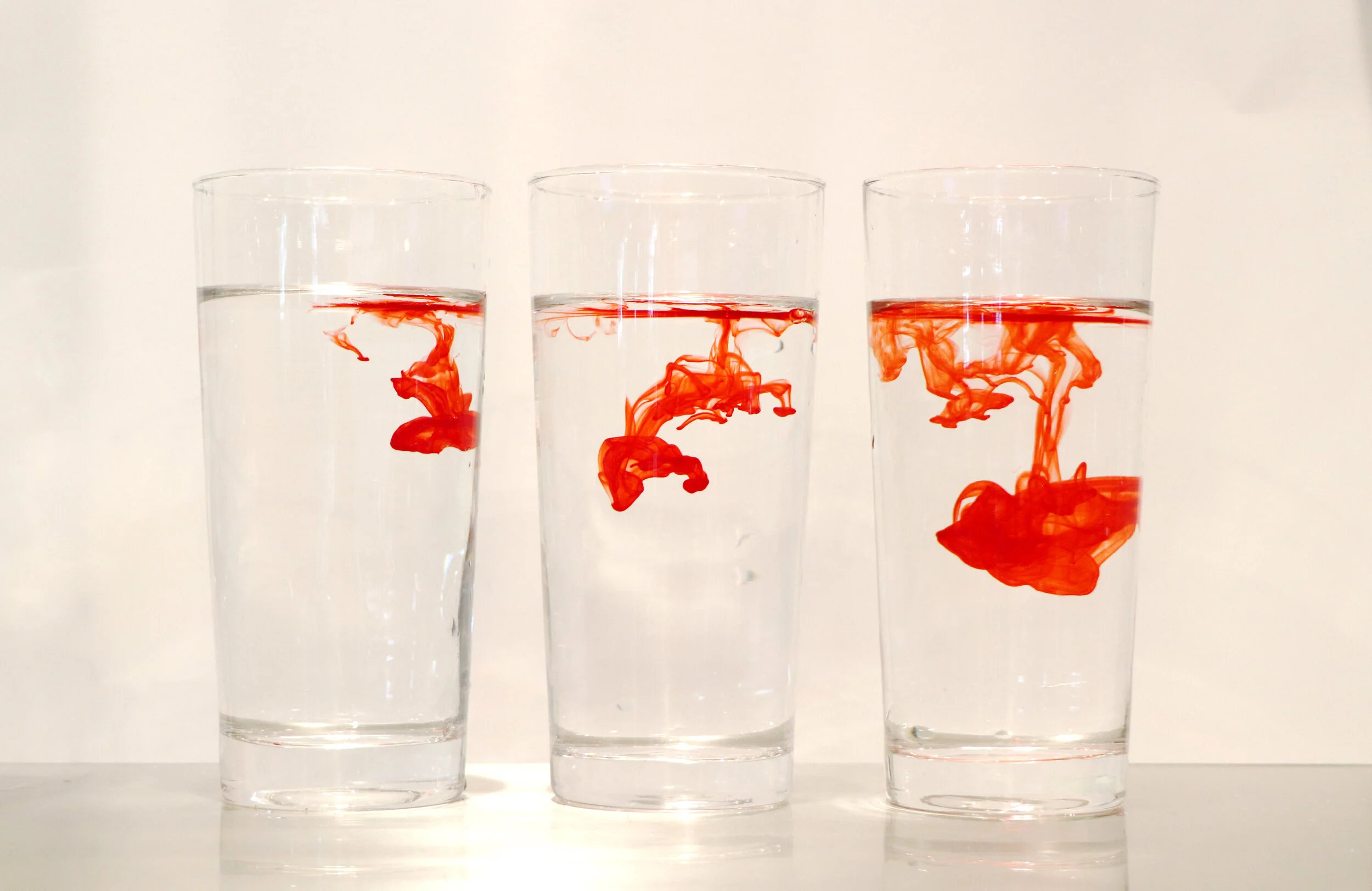 Three glasses of water with red ink moving through the water.