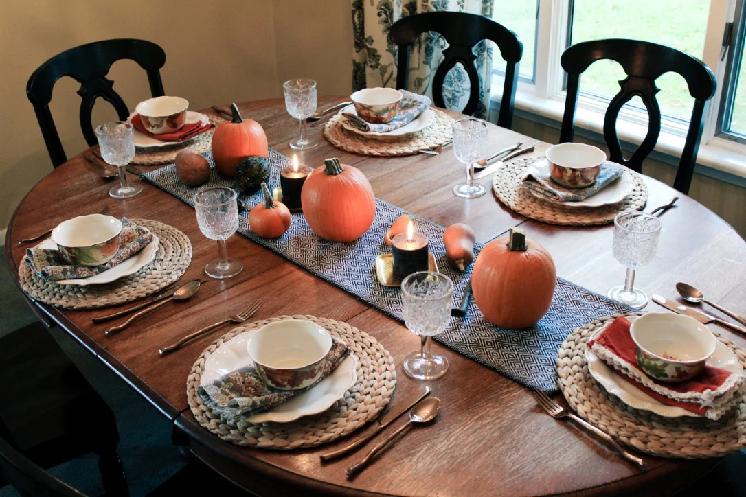 Fall harvest tablescape—table runner & placemats from Ikea, plates from Pioneer Woman (Walmart), print napkins and silverware from World Market, bowls and burnt orange napkins from HomeGoods.