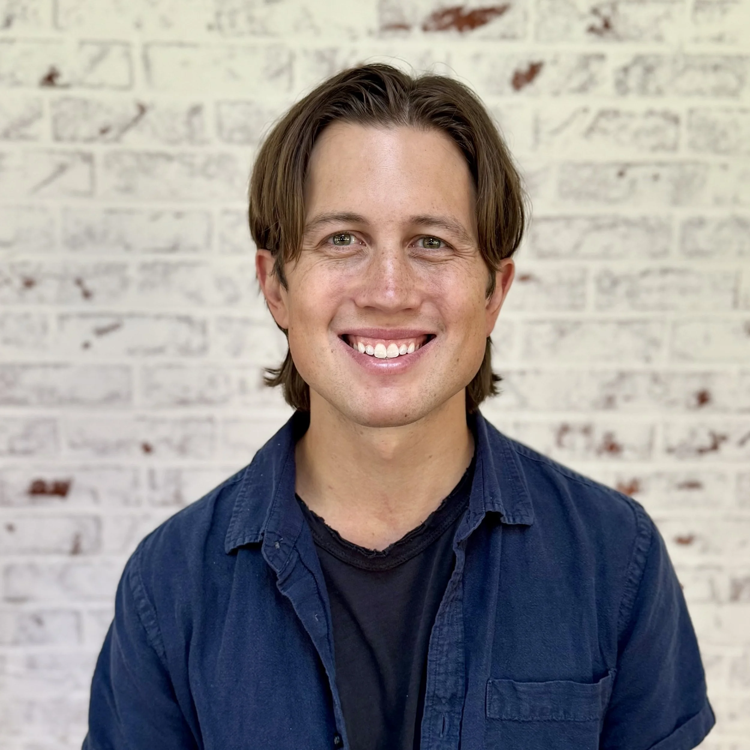 young man with brown hair and blue shirt against white brick wall