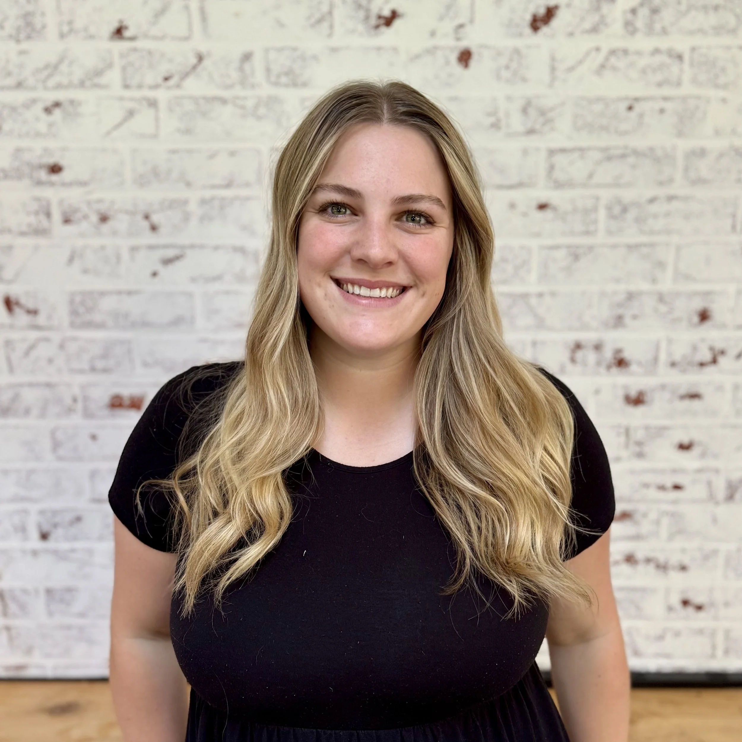 Blonde woman in black shirt against a white brick wall