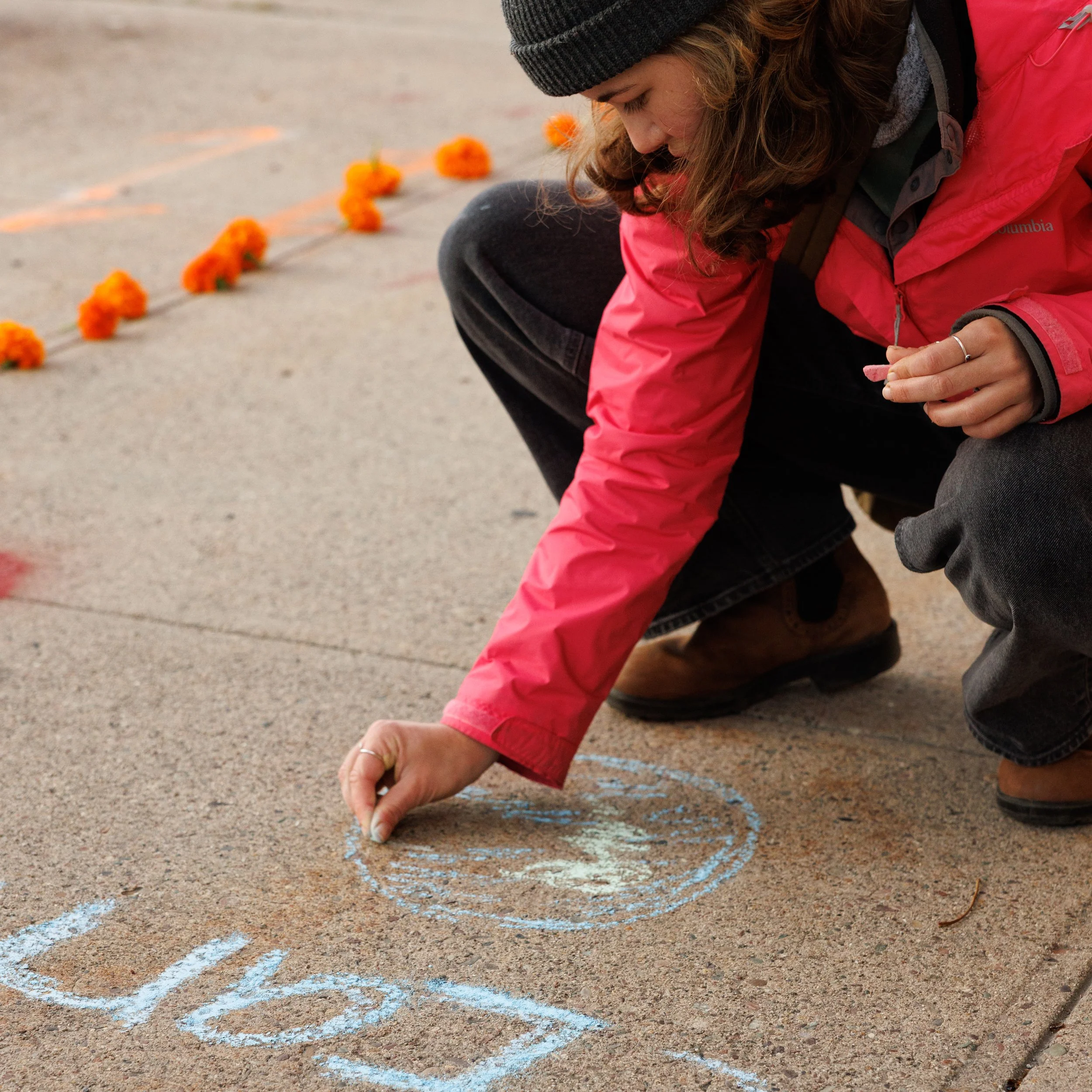 Hannah Bregman, 25, draws with chalk on the sidewalk in the lead up to the second day of trial for Lighthiser v. Trump at the Russell Smith Courthouse in Missoula, Montana on Wednesday, September 17, 2025.