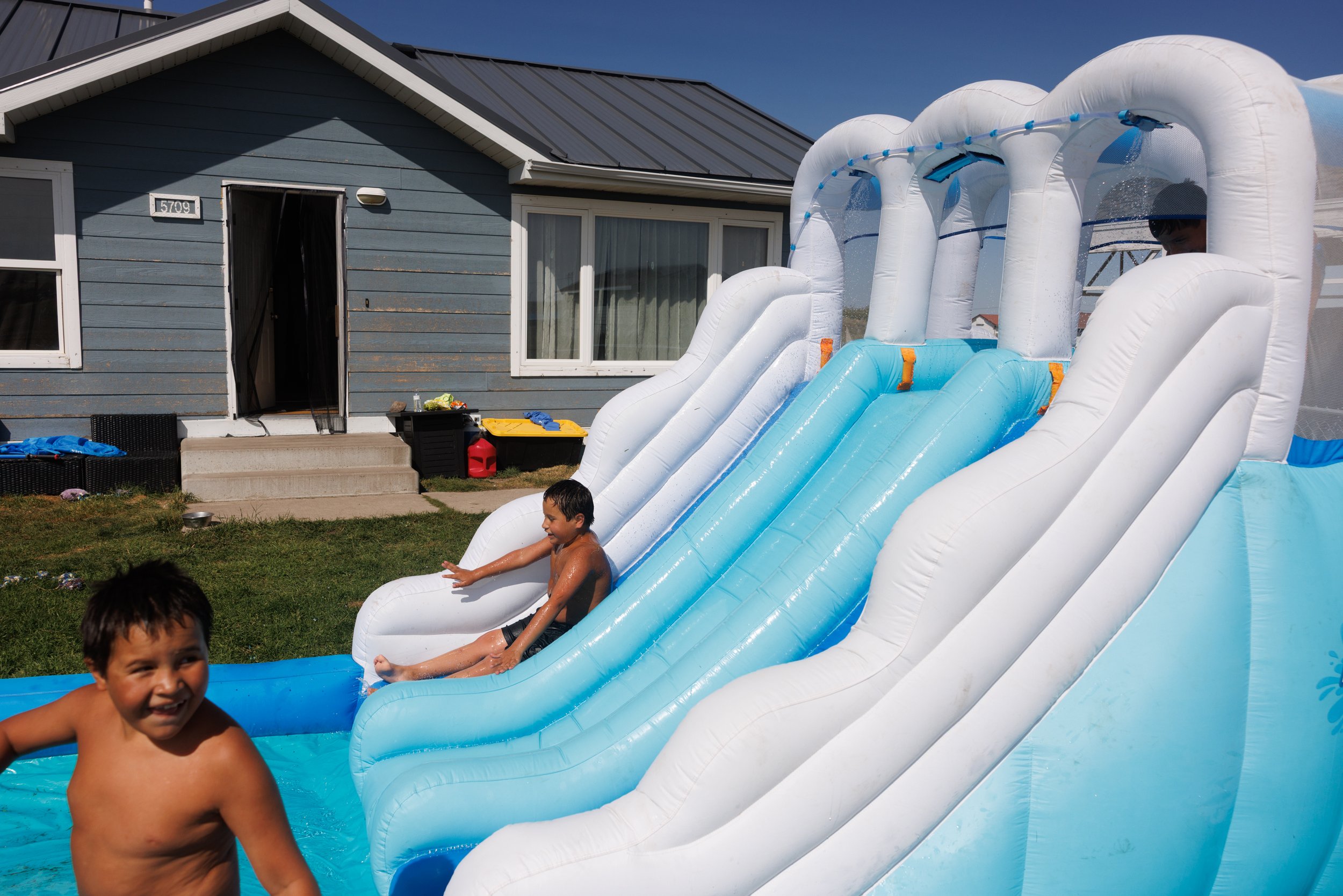 Charles Fish, 7, Linus Fish, 7, and Kenzo ArrowTop, 7, play around on a inflatable waterslide in a Rent-To-Own neighborhood on the Blackfeet Nation in Browning, Montana, on Tuesday, August 26, 2025. 