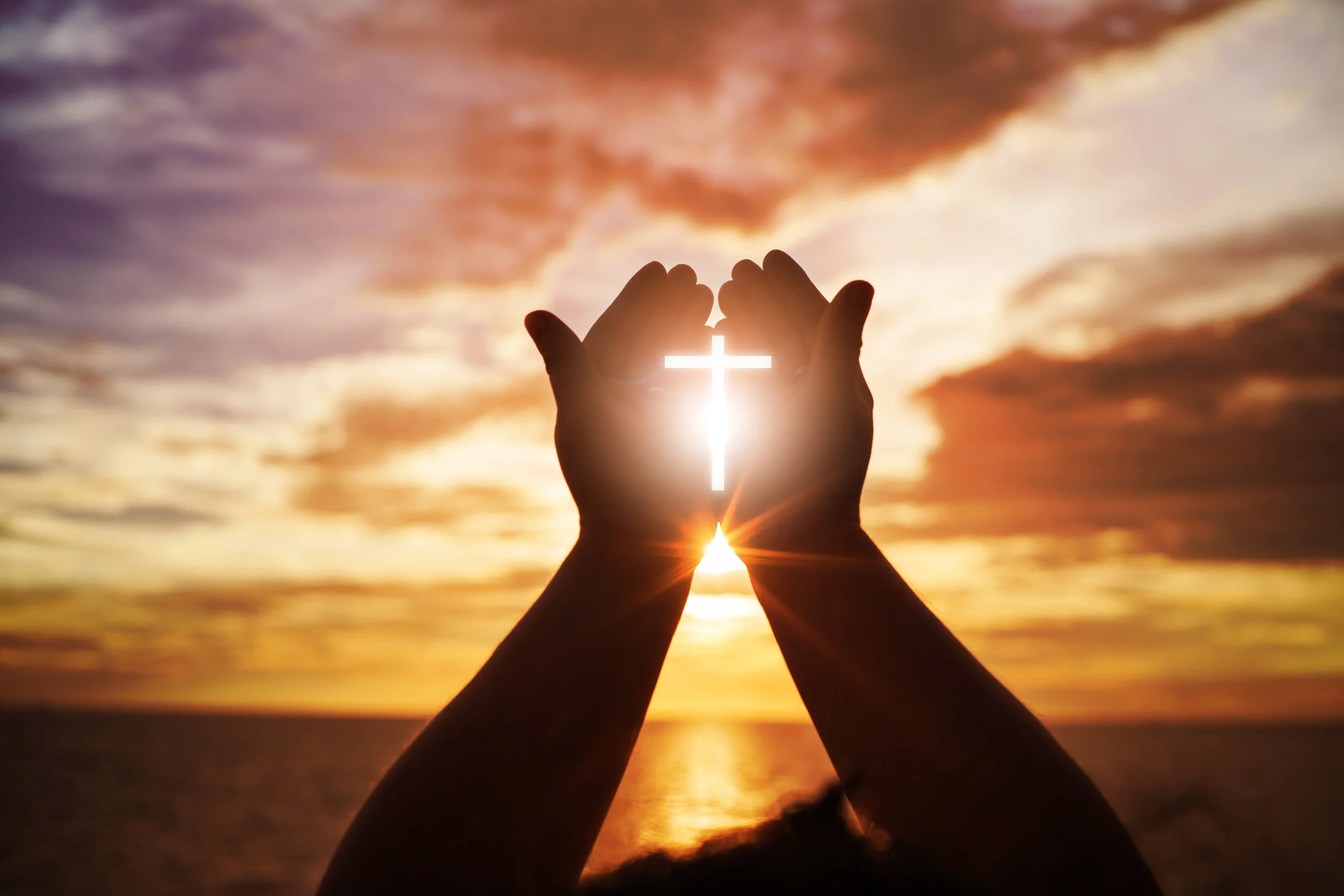 Cross held in hands against sunrise.jpg