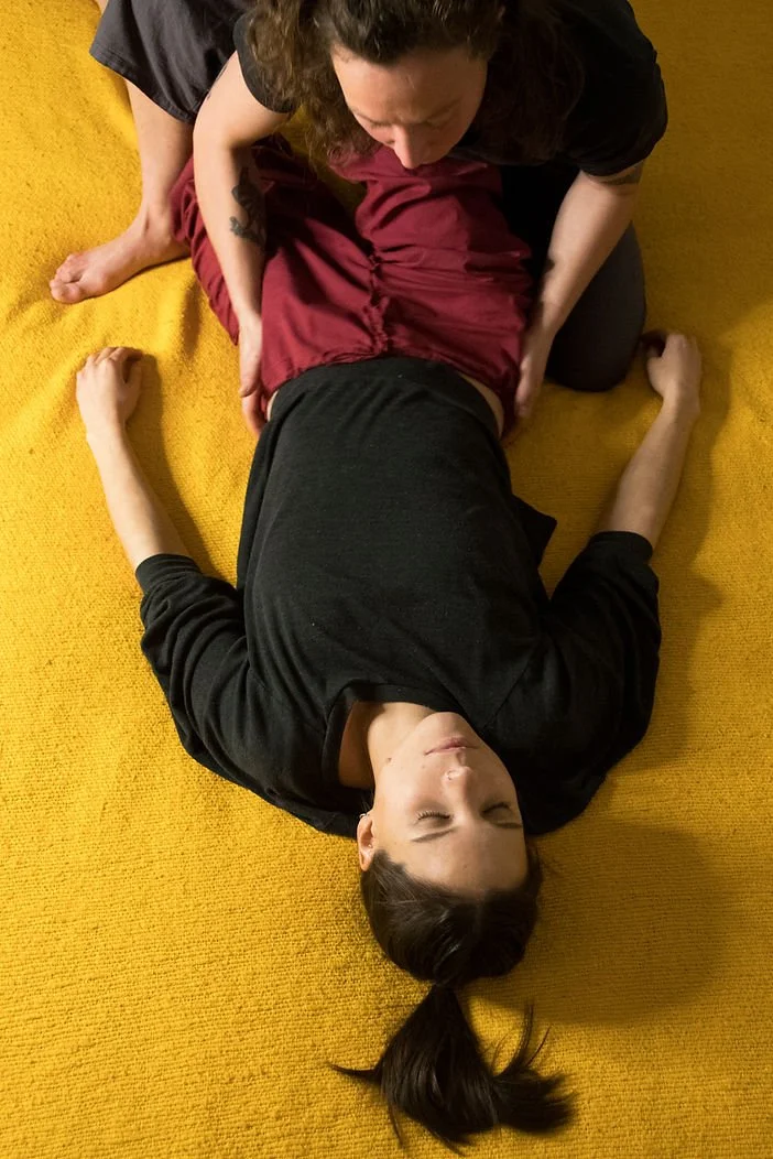 Une femme à genoux aide un homme allongé sur un tapis jaune à faire de la rééducation ou de la physiothérapie.
