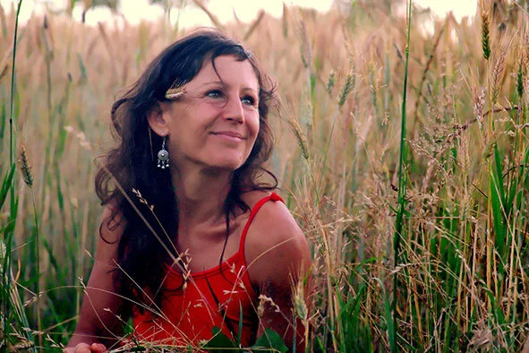 Une femme souriante portant une robe rouge, assise dans un champ de blé.