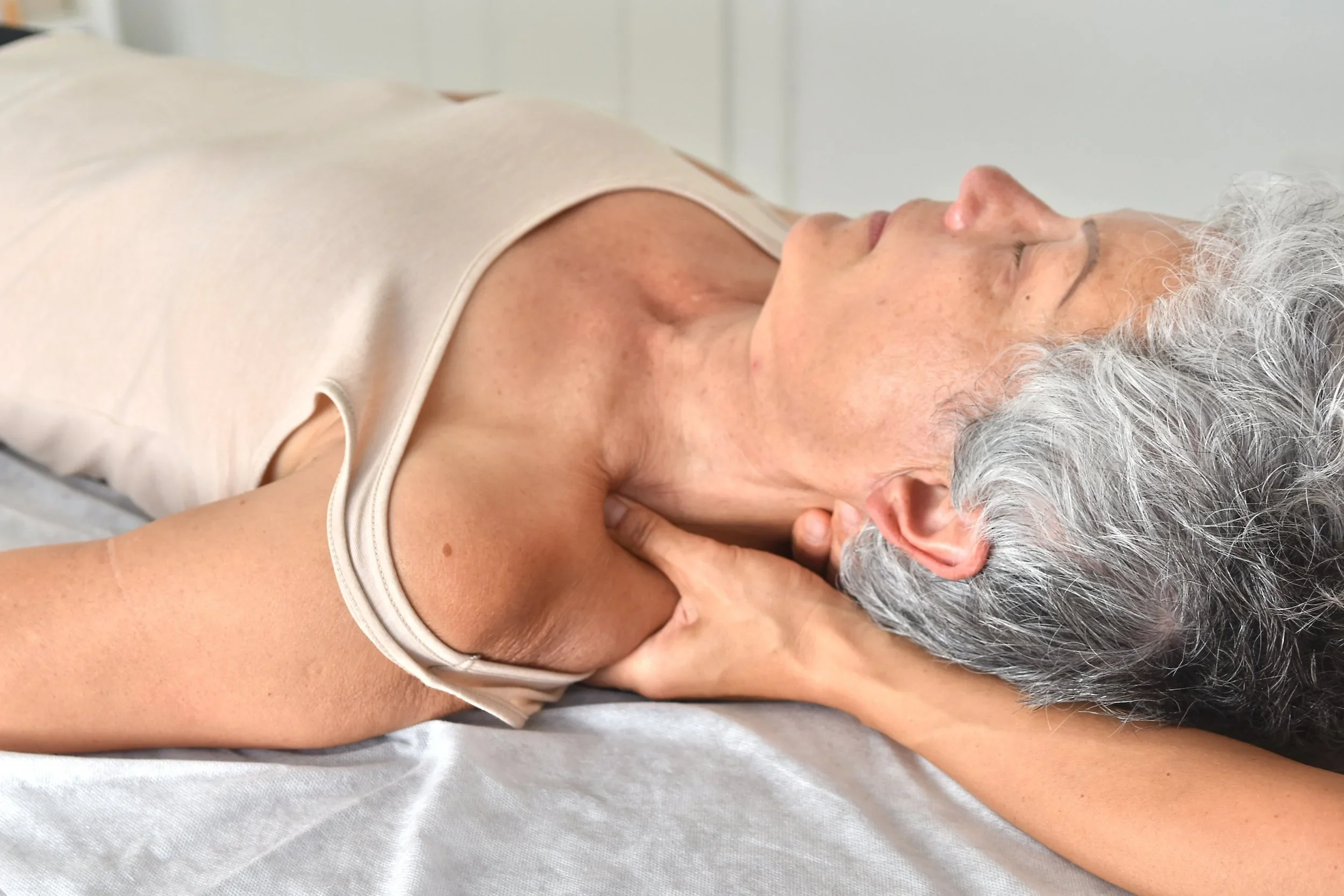 Une femme âgée recevant un massage ou une thérapie de relaxation au niveau du cou et des épaules, allongée sur un lit ou une table.