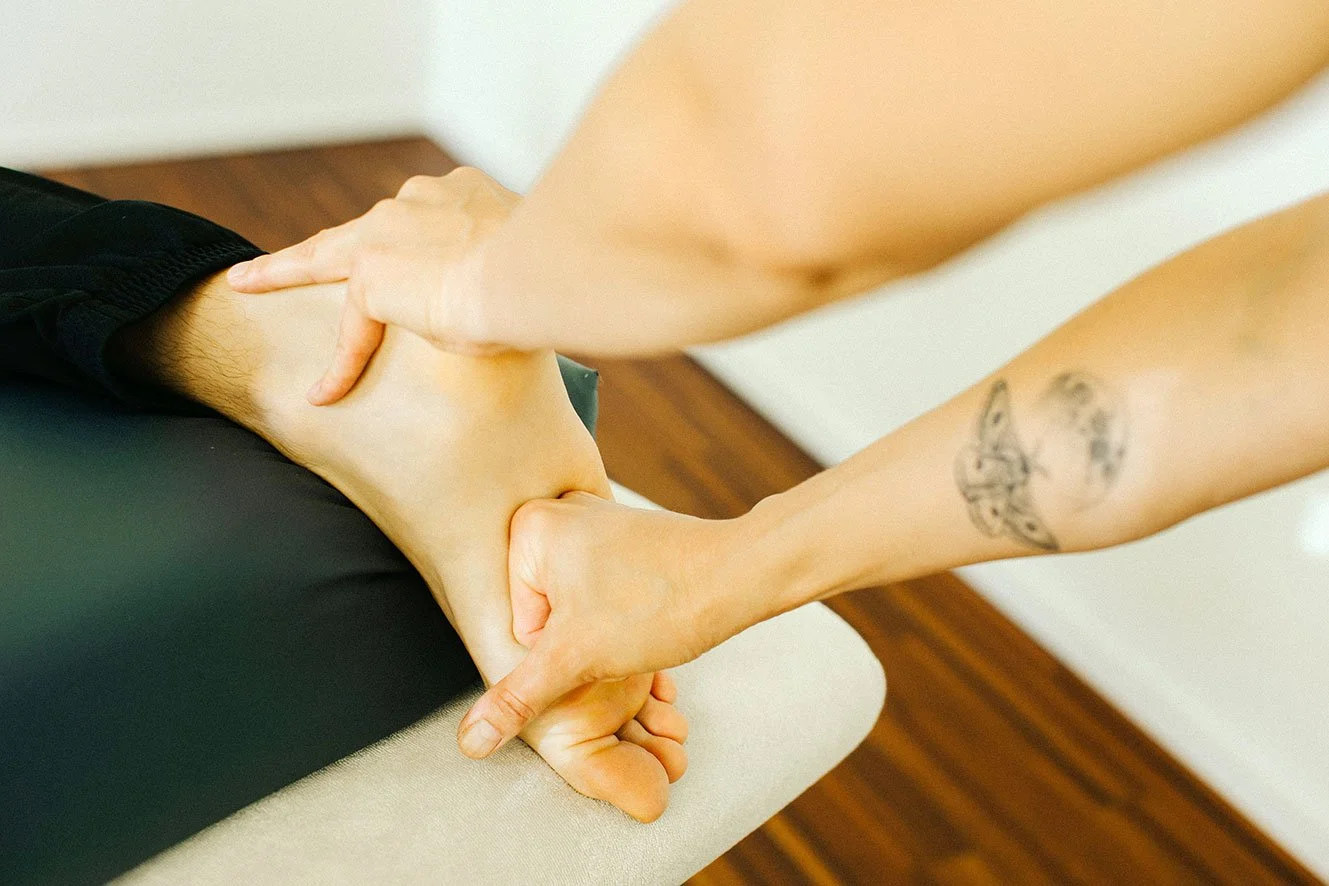 Une personne reçoit un massage ou une thérapie de la main d'un professionnel. L'image montre la main de ce professionnel manipulant la jambe ou le pied d'un autre individu.