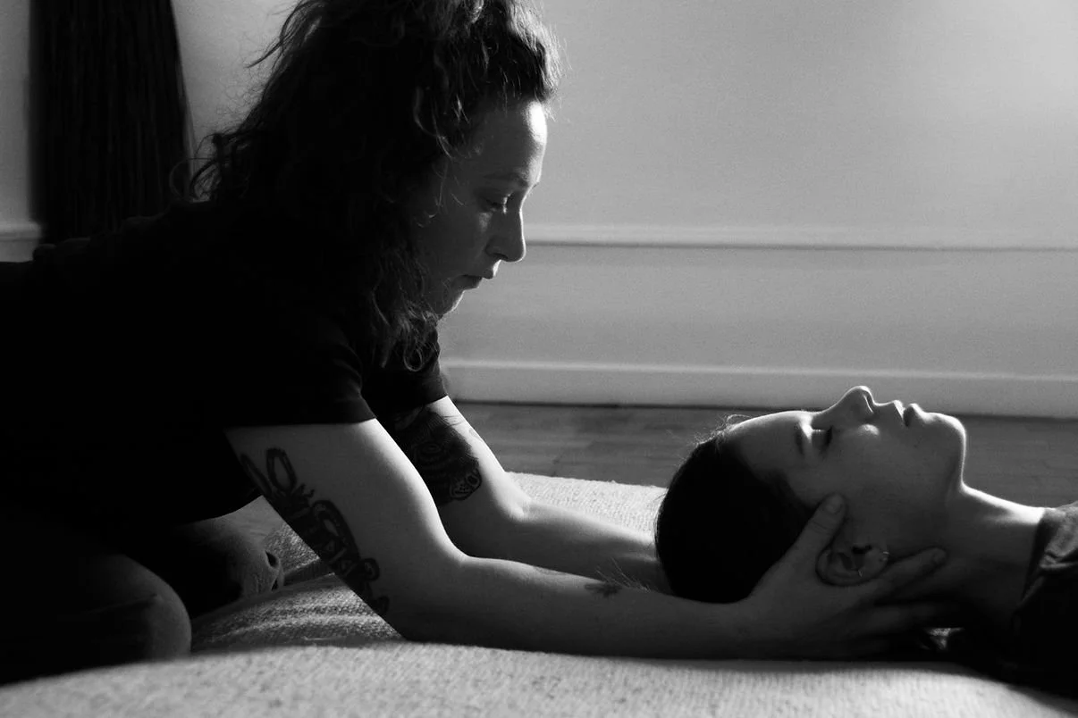 Deux femmes, une allongée et une autre à genoux, pratiquant le massage ou une séance de relaxation dans une pièce calme.