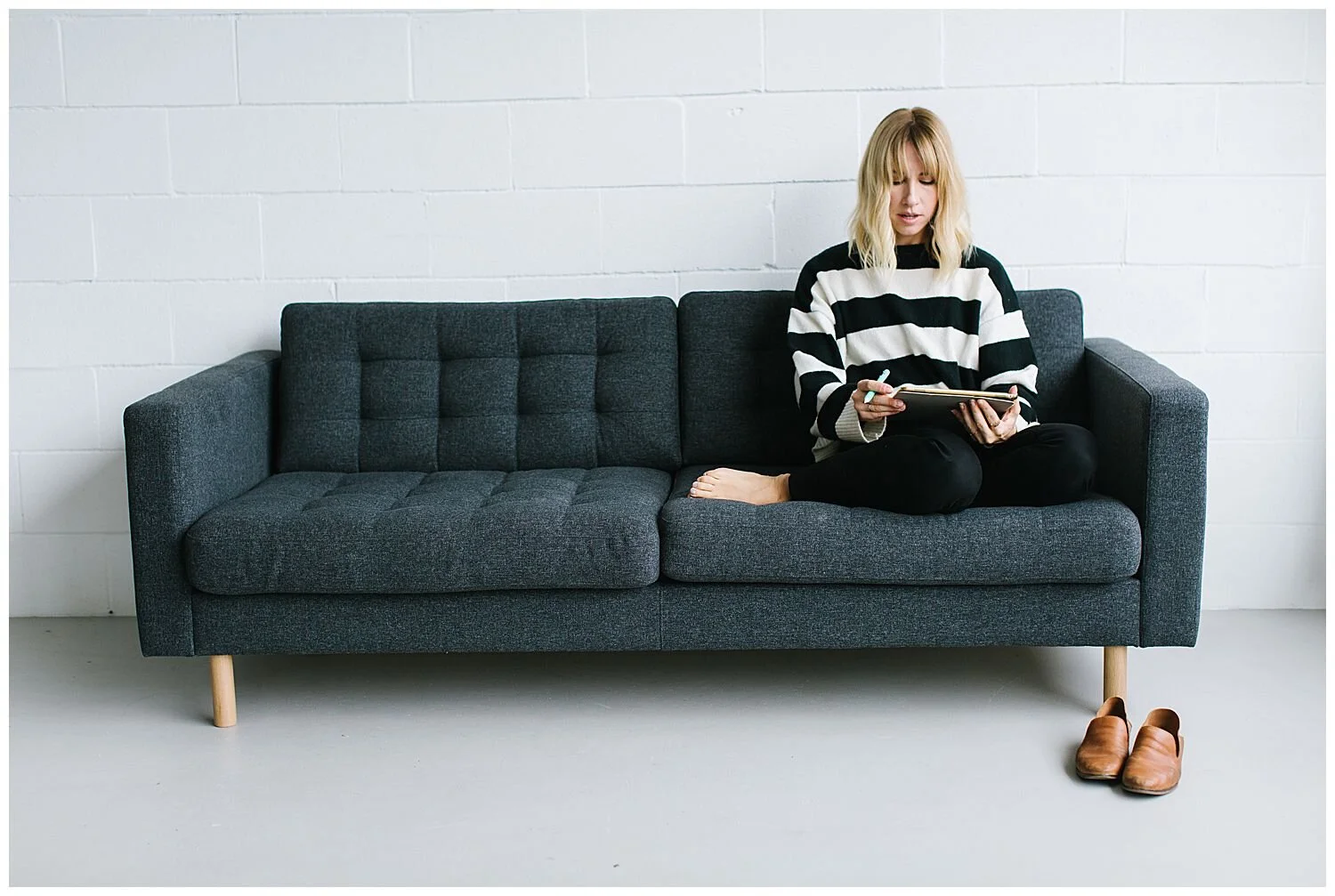 livermore lettering artists sitting on grey ikea sofa with a black and white striped sweater in front of a white brick wall at creative space studios co in livermore Ca