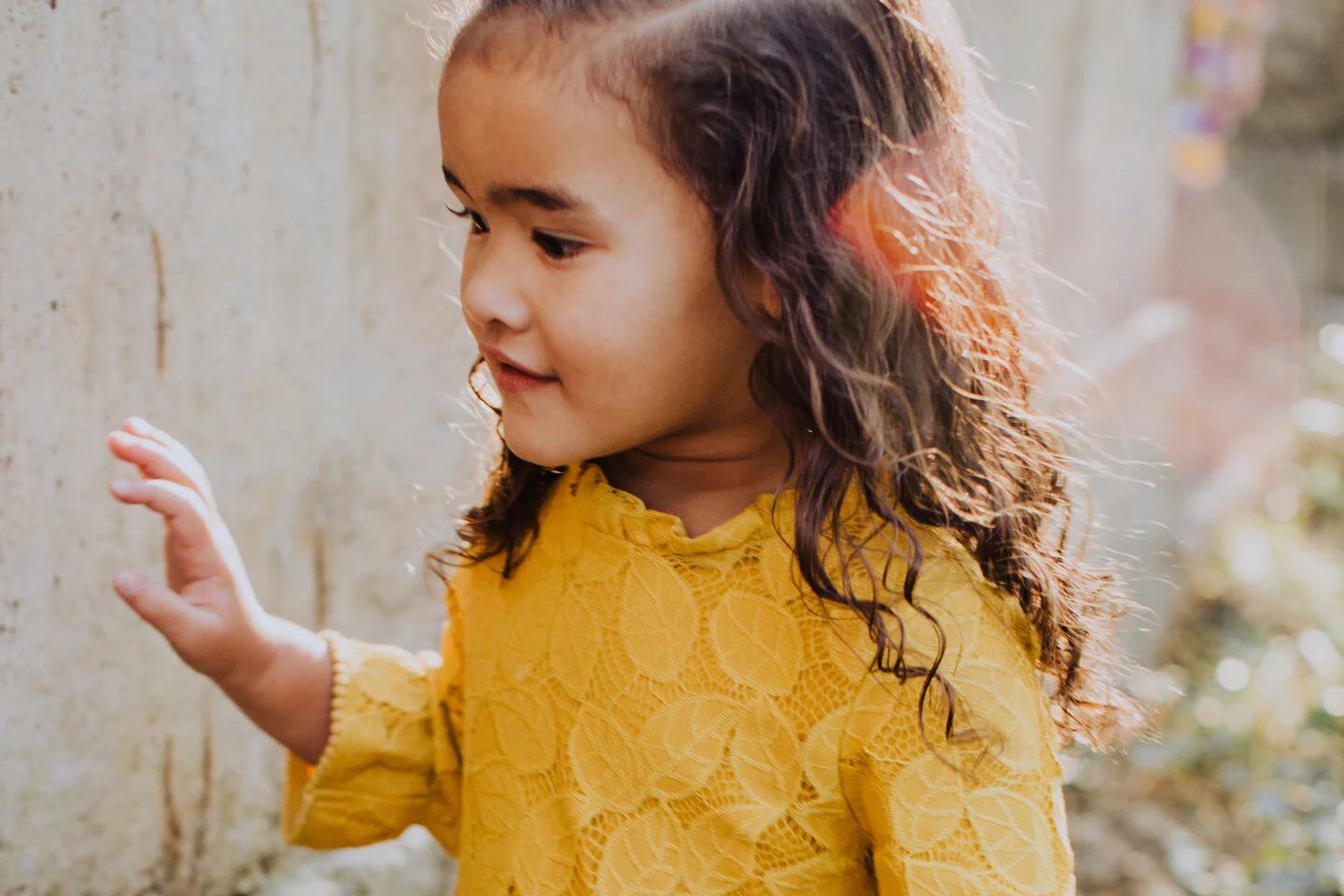 little girl in yellow lace dress running along side a concrete wall in Danville, Ca