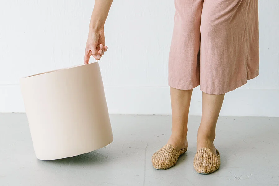 Model wearing blush pink linen pants lifting a cream planter pot standing on a concrete floor at Creative Space Studios in Danville, Ca