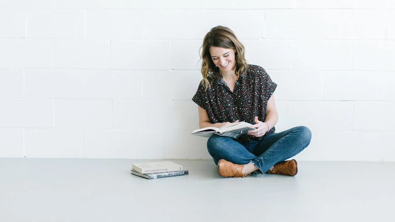 photographer-sitting-against-white-brick-wall-writing-in-leather-planner.jpg