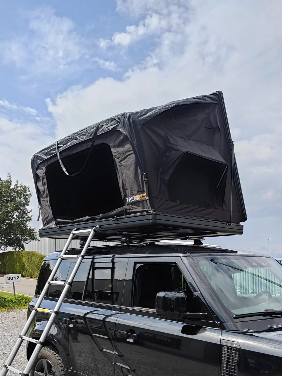 Un camping-car noir équipé d'un porte-bagages sur le toit, d'une échelle et d'une tente de toit qui se déplie.