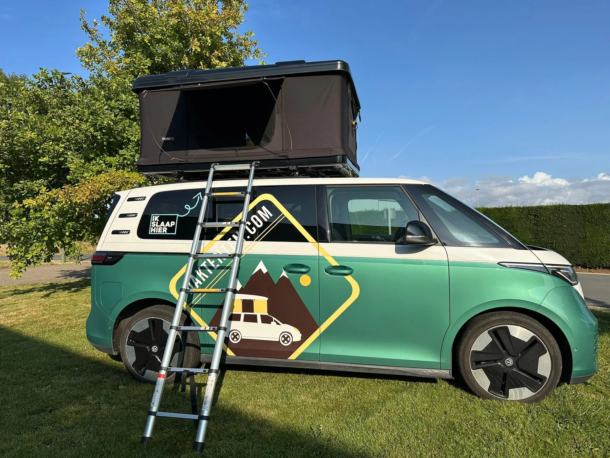 Groene en witte camper met een dak-tent, een ladder en een landschap op de achtergrond.