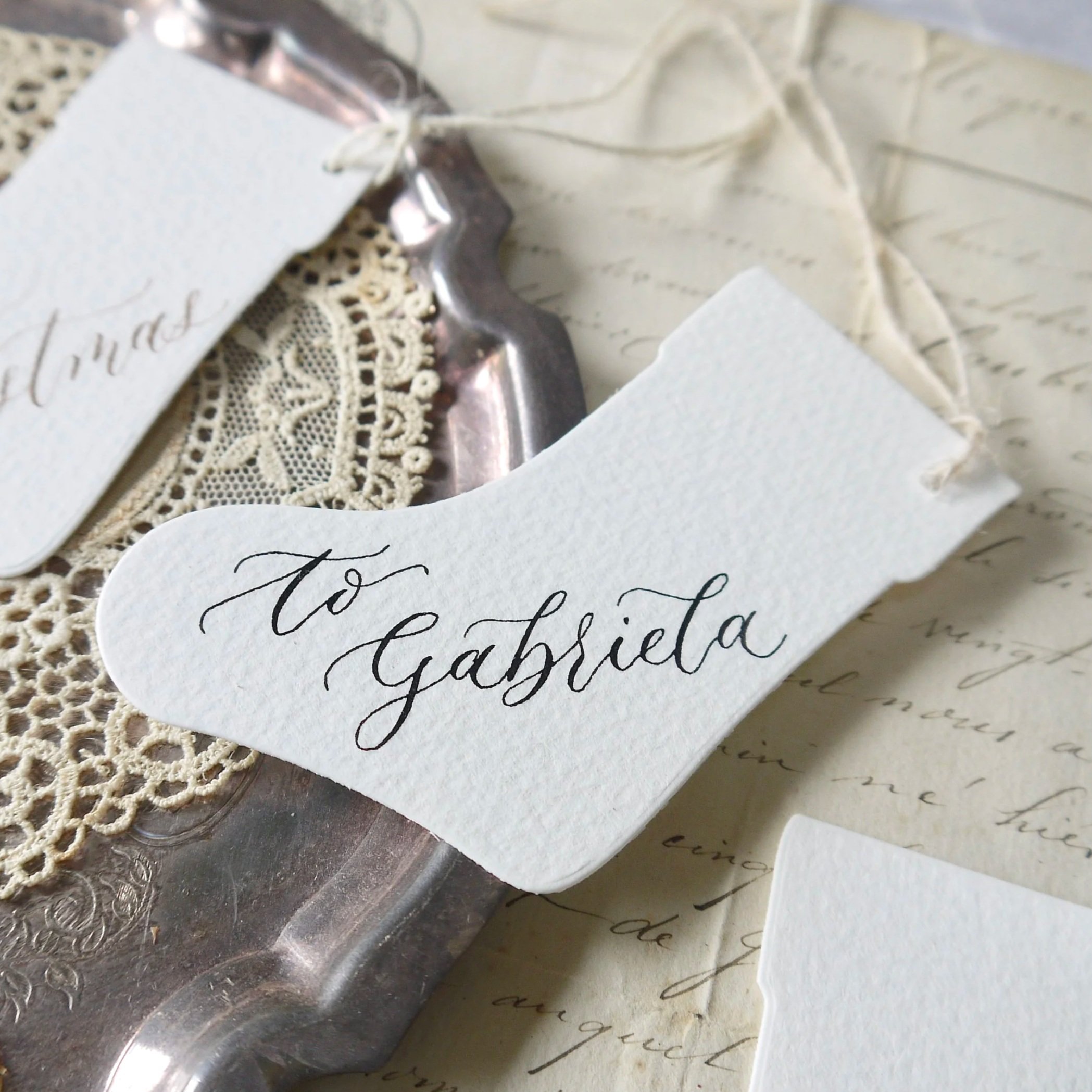 Small calligraphy Christmas tag reading ‘To Gabriella’ in crimson ink, styled with festive décor.