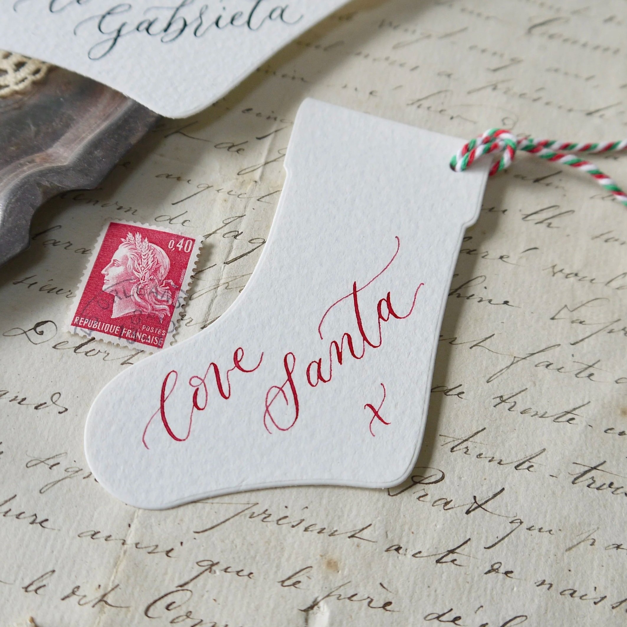 Handwritten personalised Christmas gift tag with twine, displayed on textured off-white paper