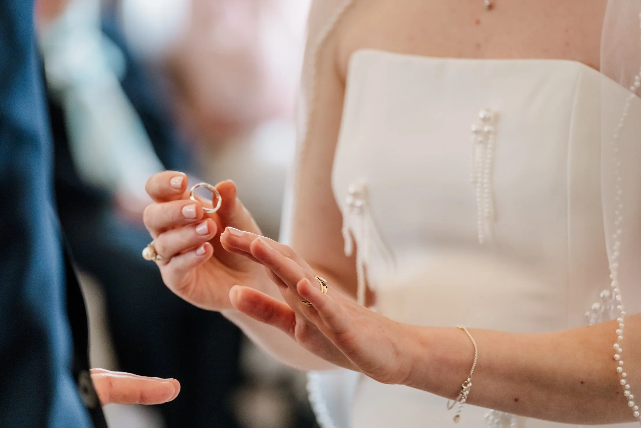 Close-up of a bride holding a wedding ring, with an “I do” gesture, during a wedding ceremony.