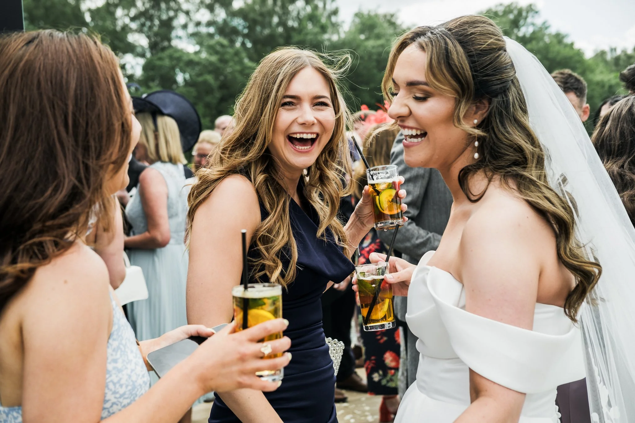 A group of women at a wedding celebration outdoors, holding glasses of drinks and laughing.