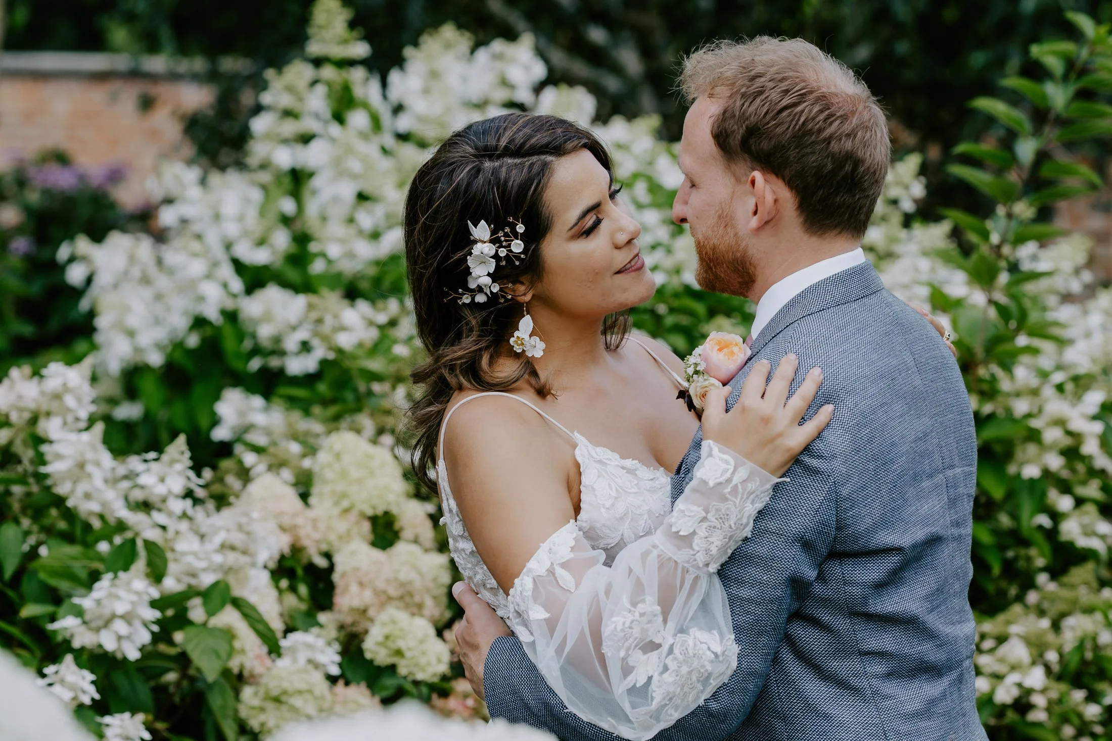 A bride and groom sharing an intimate moment outdoors with lush green foliage and white flowers in the background.