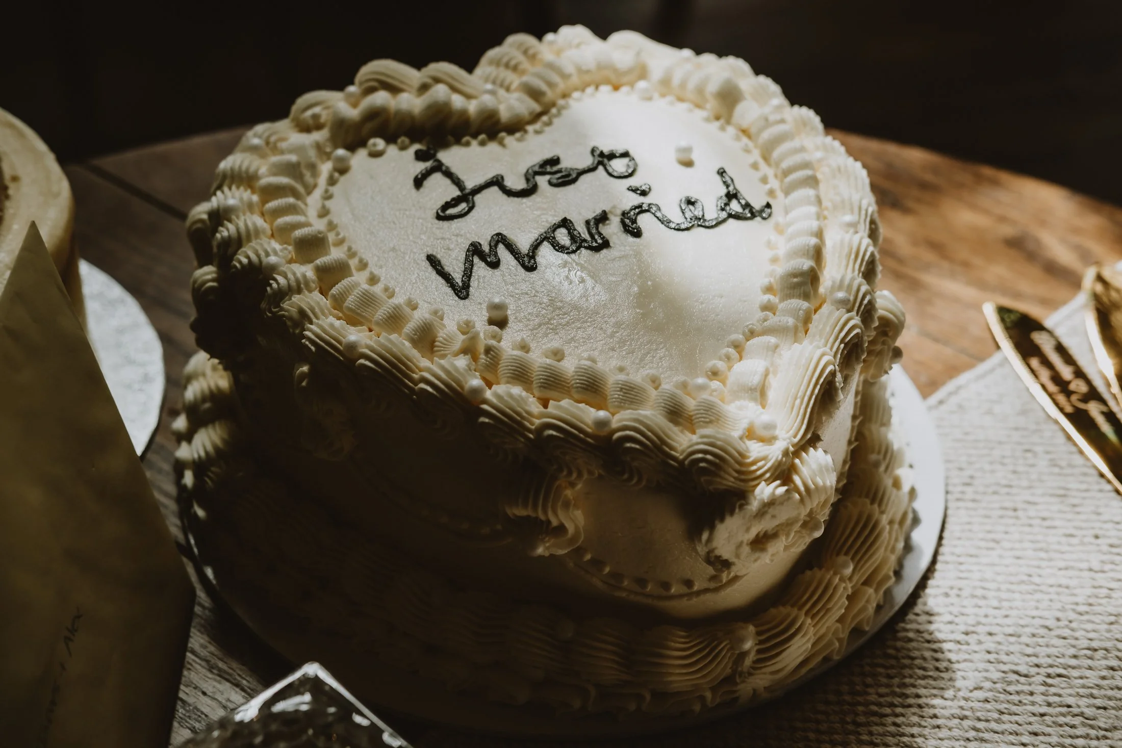 A heart-shaped wedding cake with white icing and piped decorations, with the words 'been married' written on top in black icing, placed on a wooden table.
