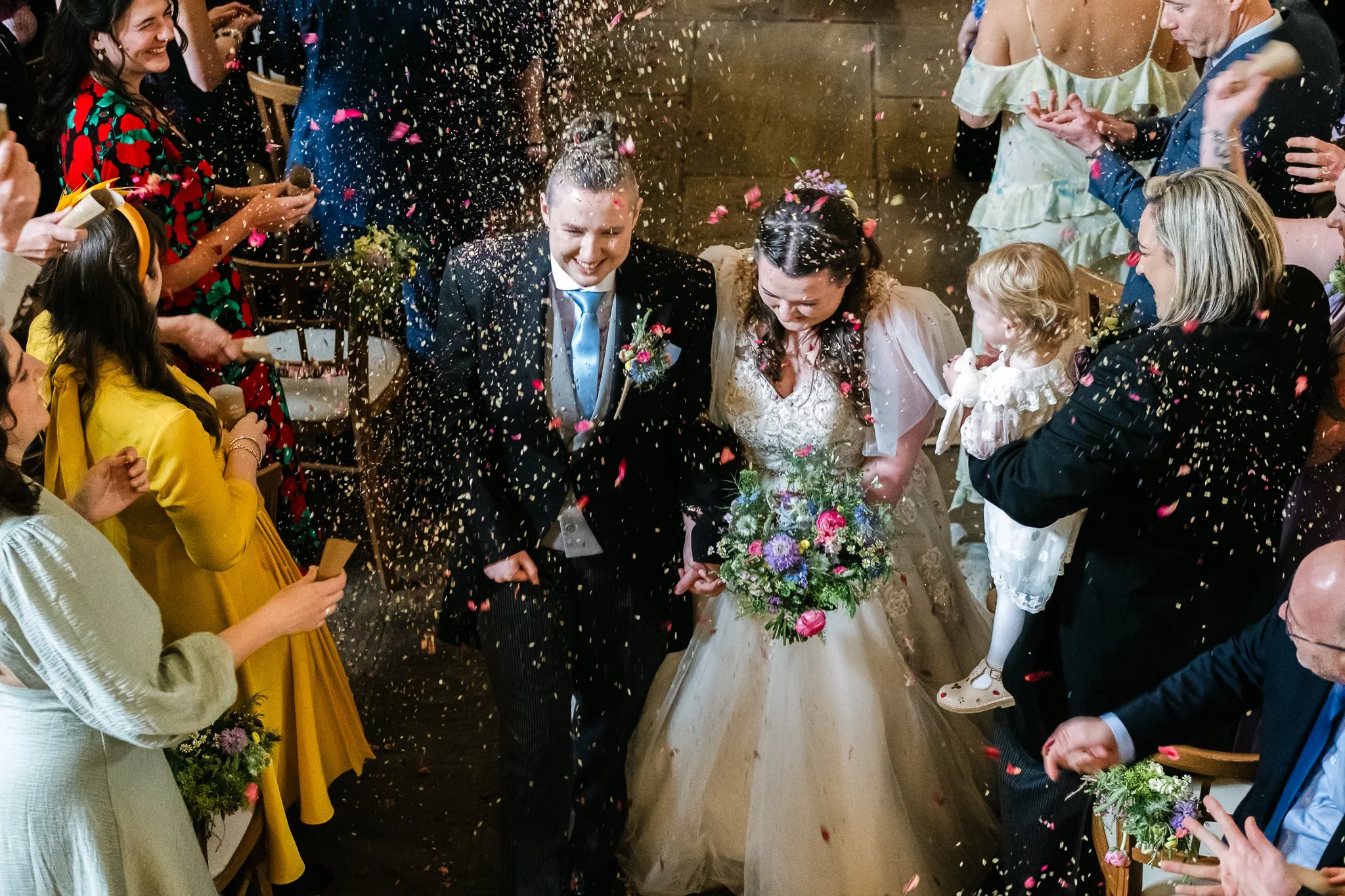 Happy wedding couple walking through confetti with guests celebrating around them.
